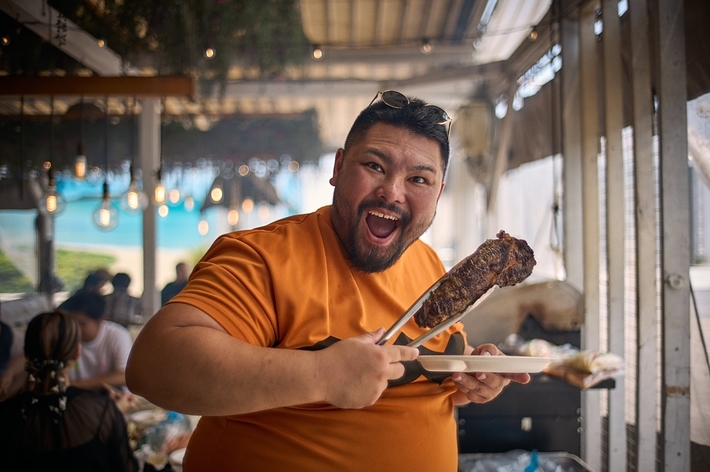 屋外の食事会でバーベキューをしている笑顔の男性。