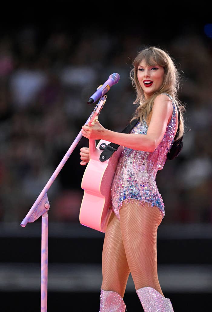 Taylor Swift performing on stage with an acoustic guitar, wearing a sparkling bodysuit and knee-high boots