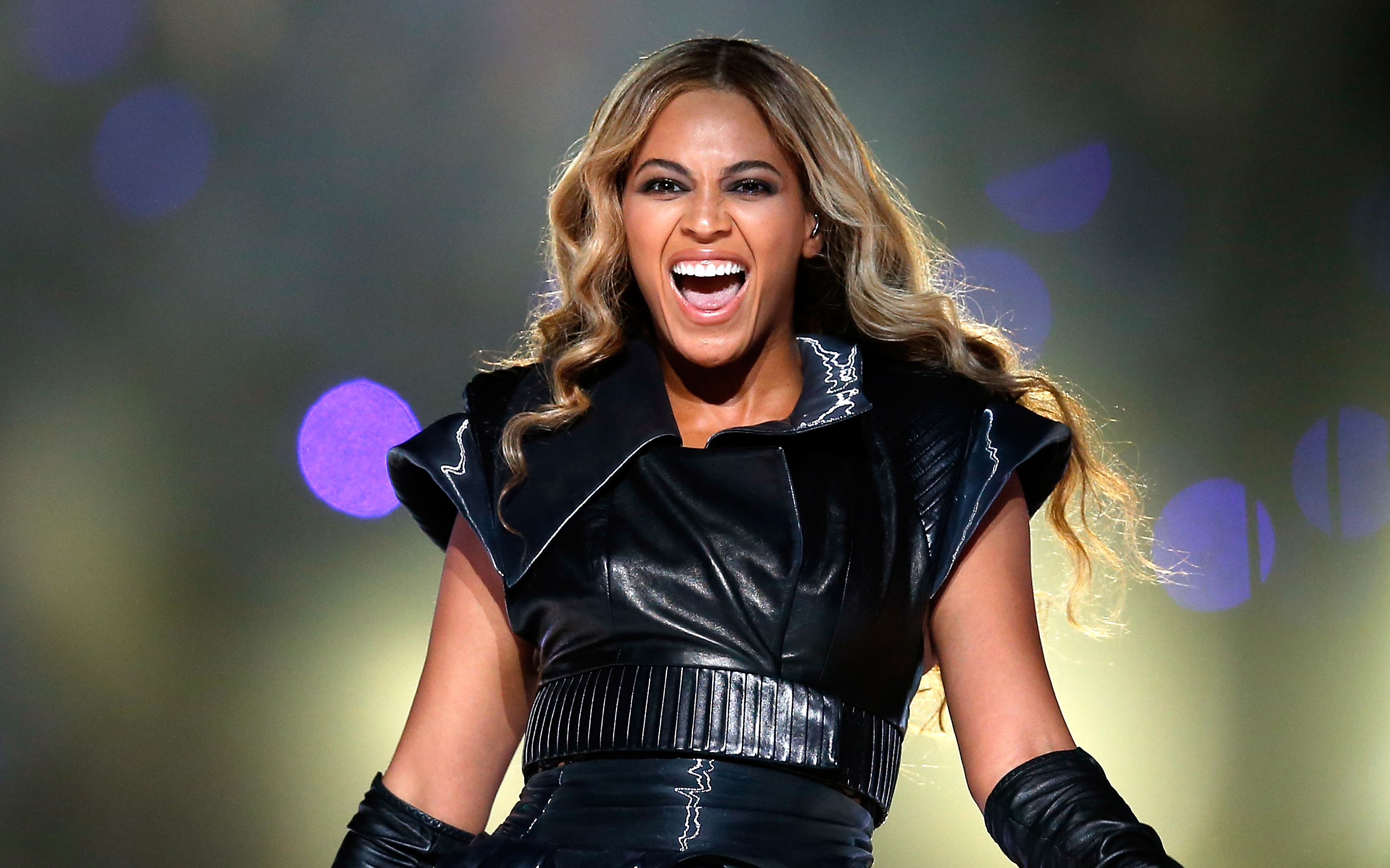 Beyoncé performing on stage, wearing a stylish black leather outfit and smiling energetically