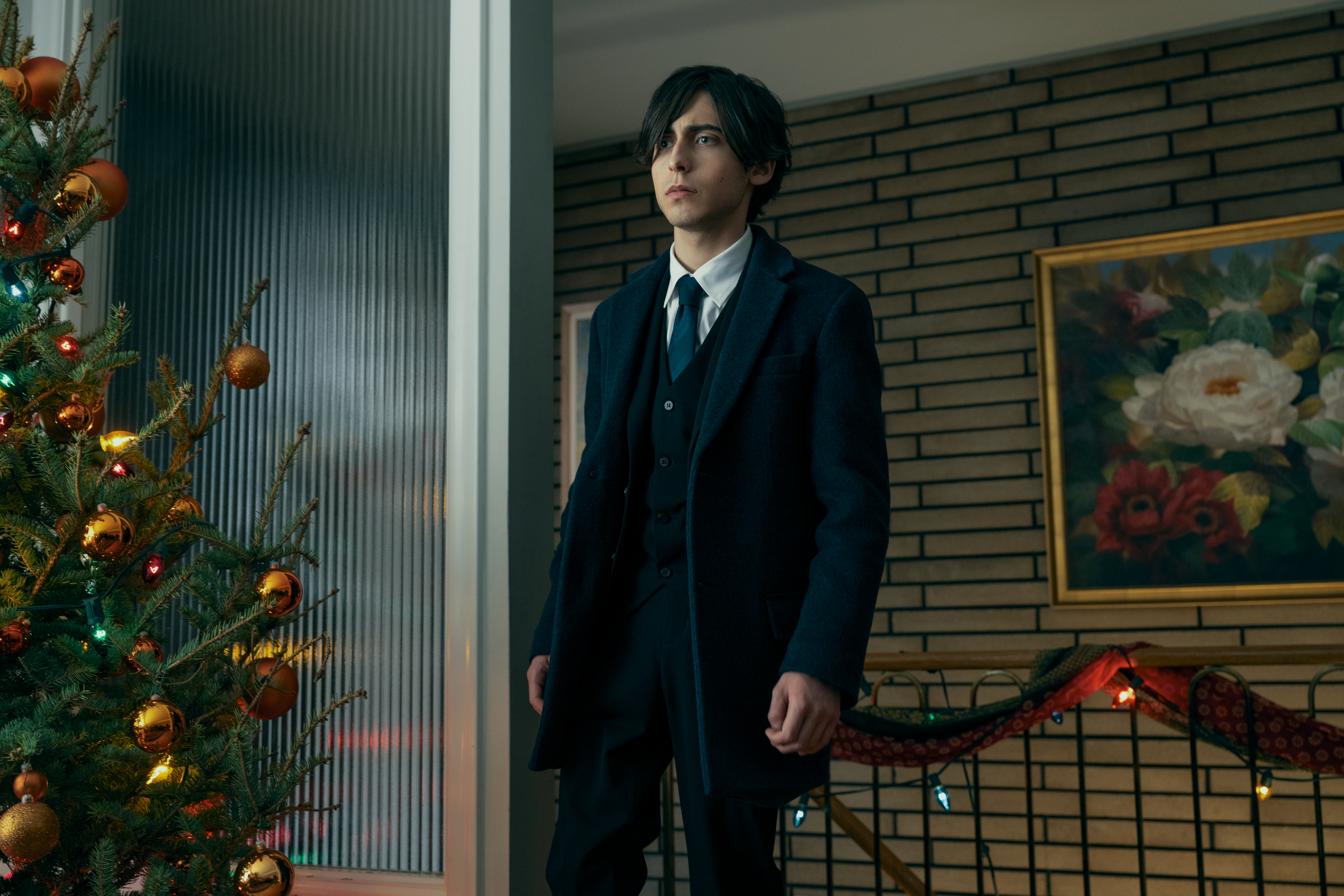 Aidan Gallagher as Number Five from The Umbrella Academy stands near a decorated Christmas tree inside a modern home