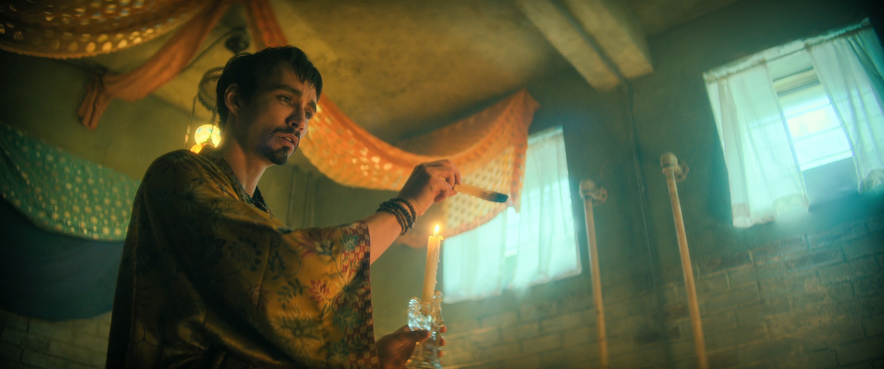 Robert Sheehan wearing a robe and holding a candle with drapes in the background in a scene from "The Umbrella Academy"