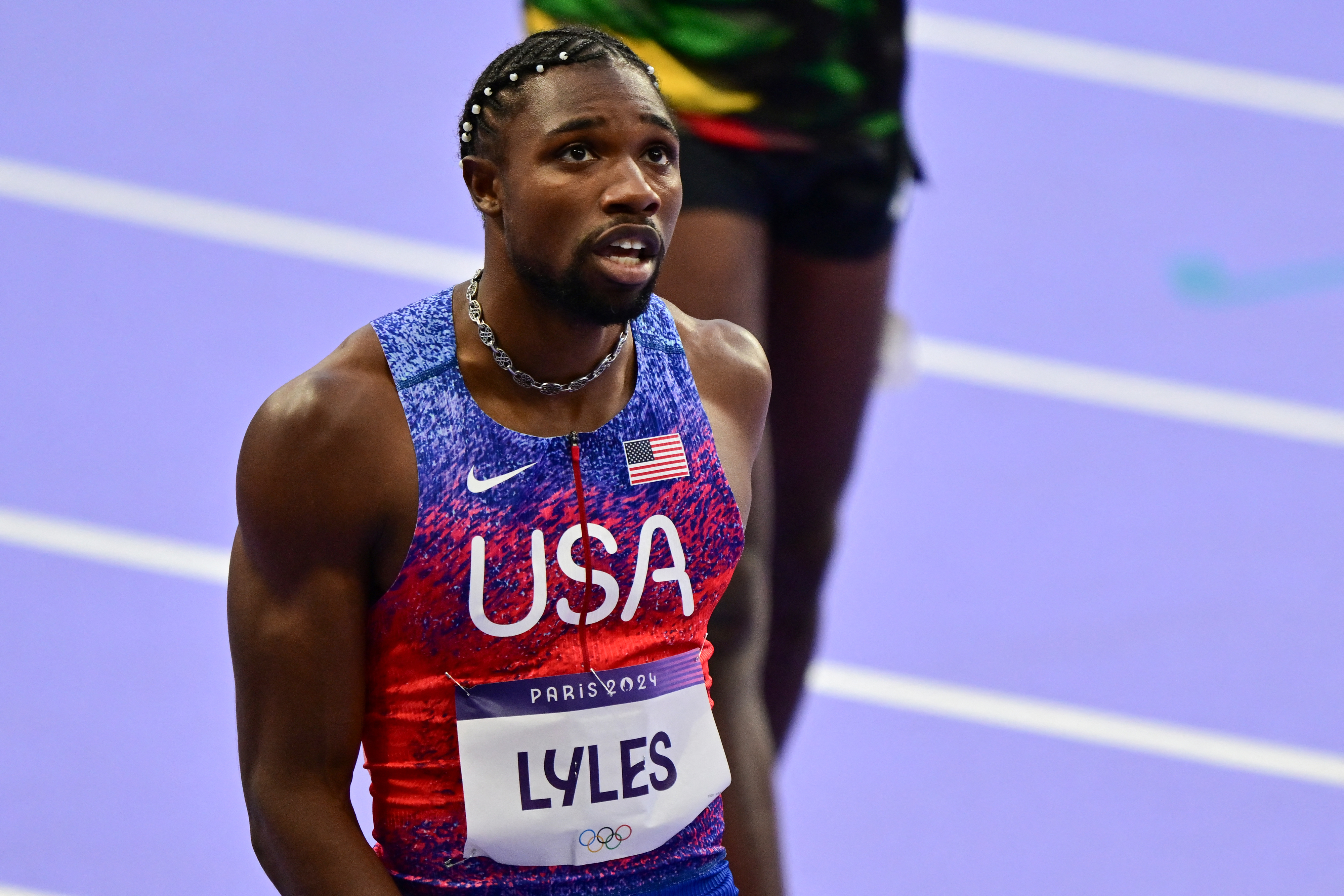 Noah Lyles on the track in a USA jersey, wearing a race bib with &quot;LYLES&quot; at an athletic event