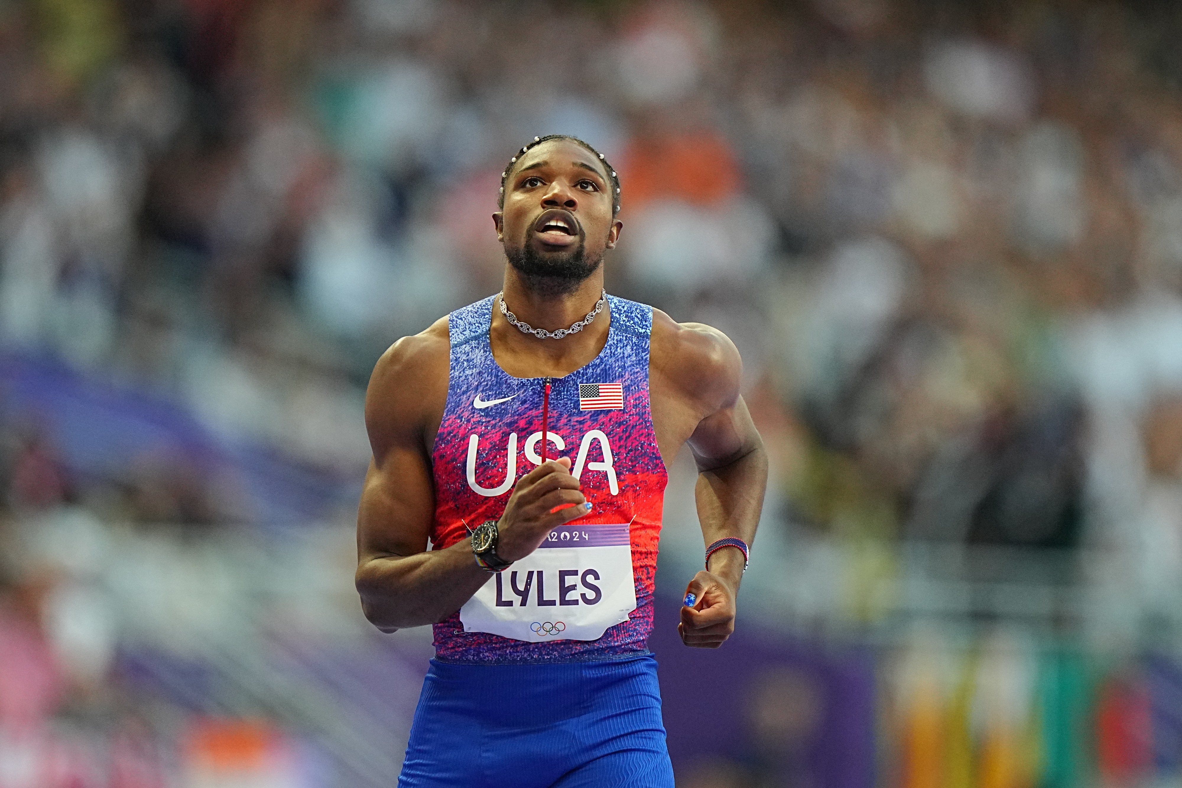 Noah Lyles in a USA uniform, running during an athletics event, with a focused expression