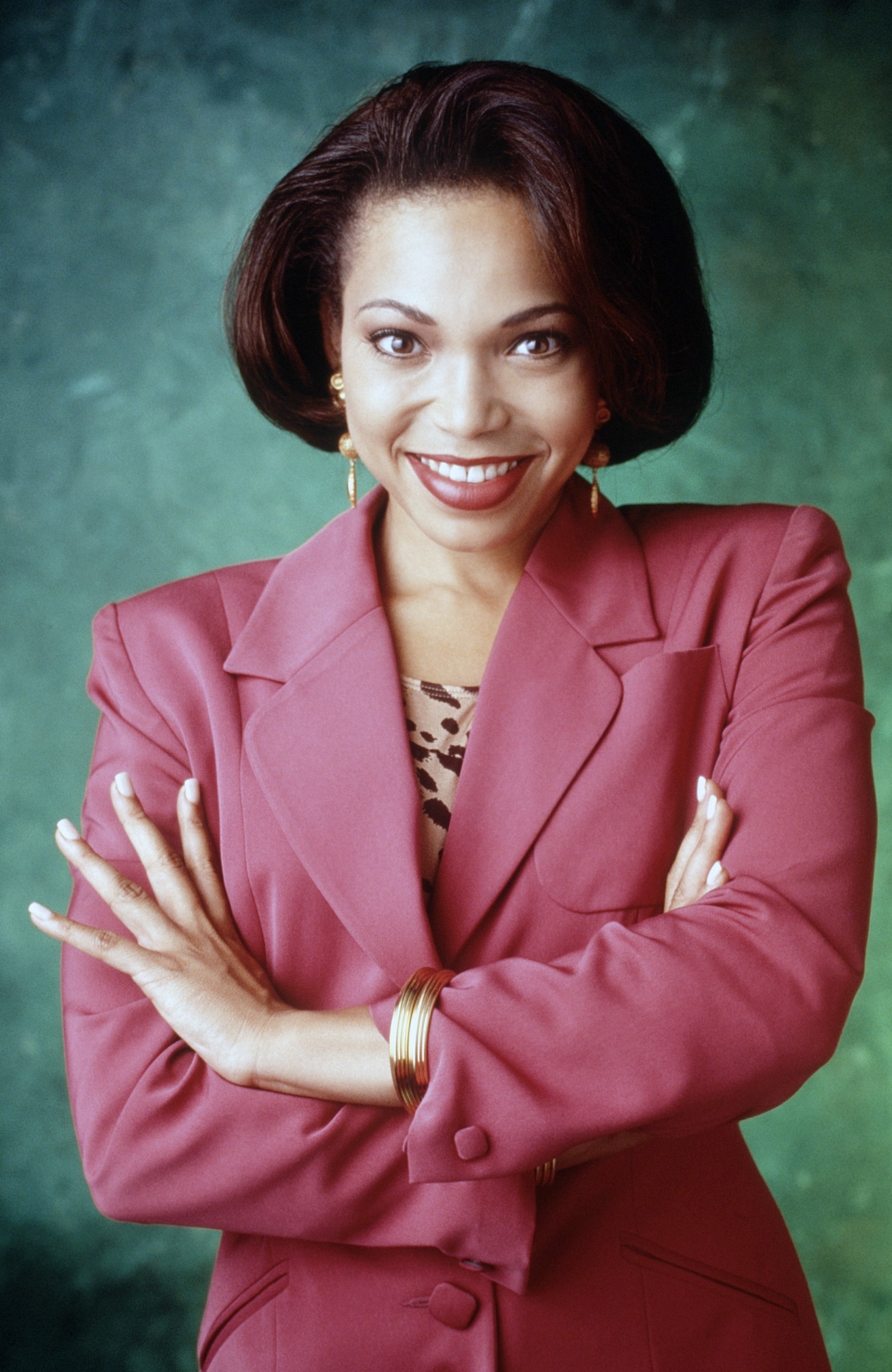 Tichina Arnold smiling with arms crossed, wearing a suit jacket over a leopard print top, with gold hoop earrings and matching bracelets