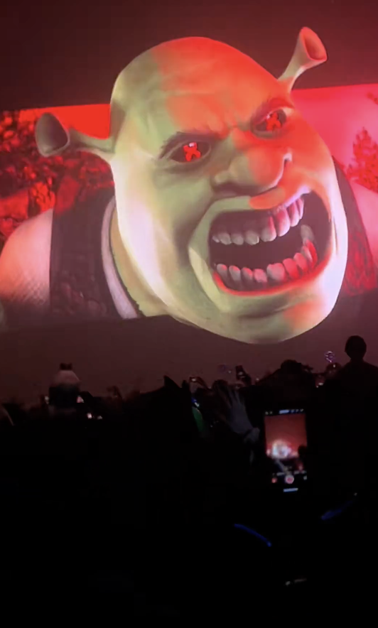 People attending an event with a large screen projection of Shrek in an enraged expression