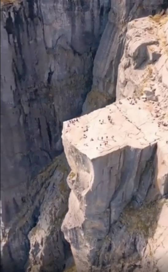Aerial view of a large group of people gathered on a steep, dramatic cliff edge, likely a popular tourist spot