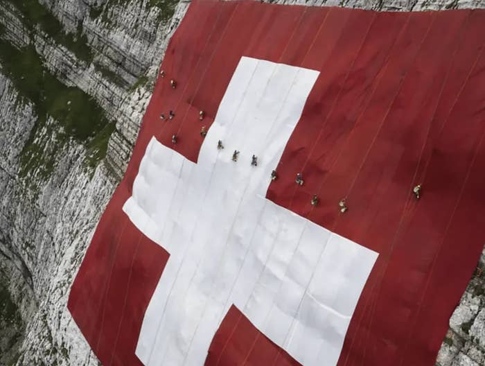 People climb across a massive Swiss flag spread over a mountainside, showcasing a breathtaking blend of human endeavor and natural beauty