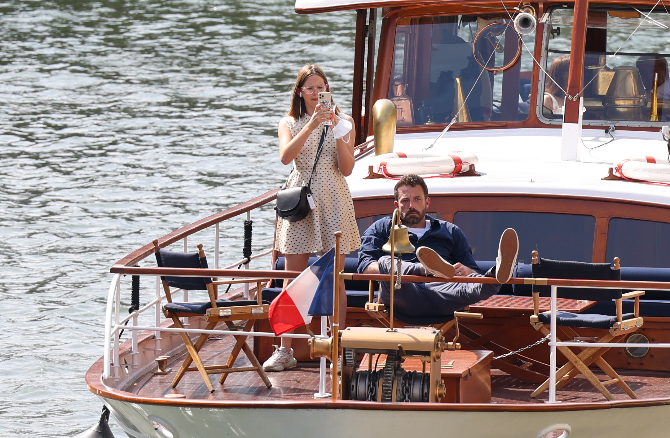 Violet Affleck and Ben Affleck are on a boat. Jennifer is standing and taking a photo, while Adam is lounging with his feet up
