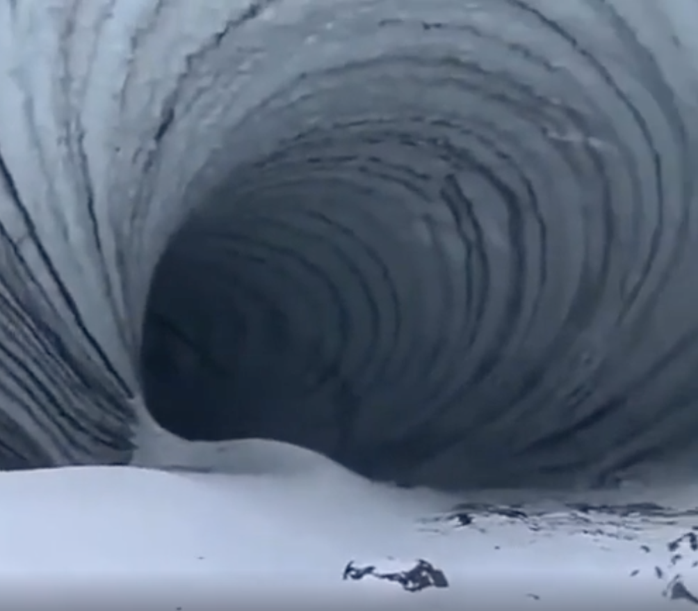 Large, spiral ice tunnel leading into darkness, surrounded by snow and ice