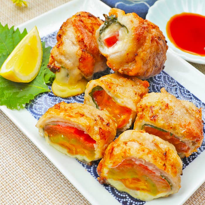 皿に盛られた肉で巻かれた野菜とチーズの揚げ物、付け合せのレモンと醤油皿が見えます。