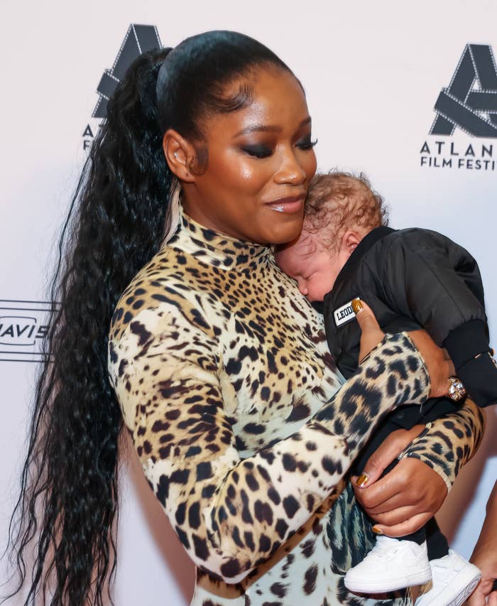 Keke Palmer holding an infant at the Atlanta Film Festival. She wears a leopard-print dress, and the baby is dressed in black