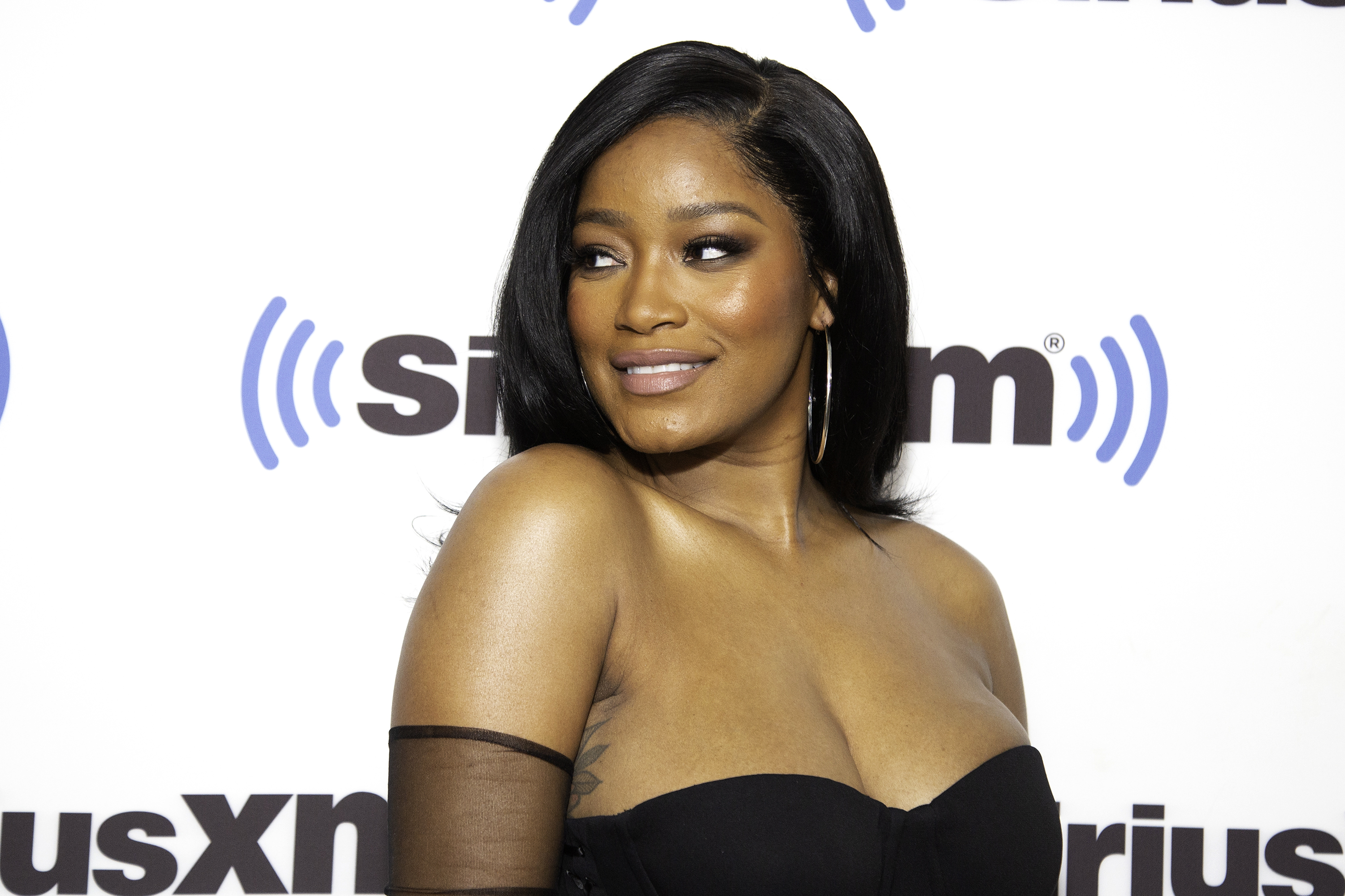 Keke Palmer on the red carpet at a SiriusXM event, wearing an off-shoulder black dress and hoop earrings