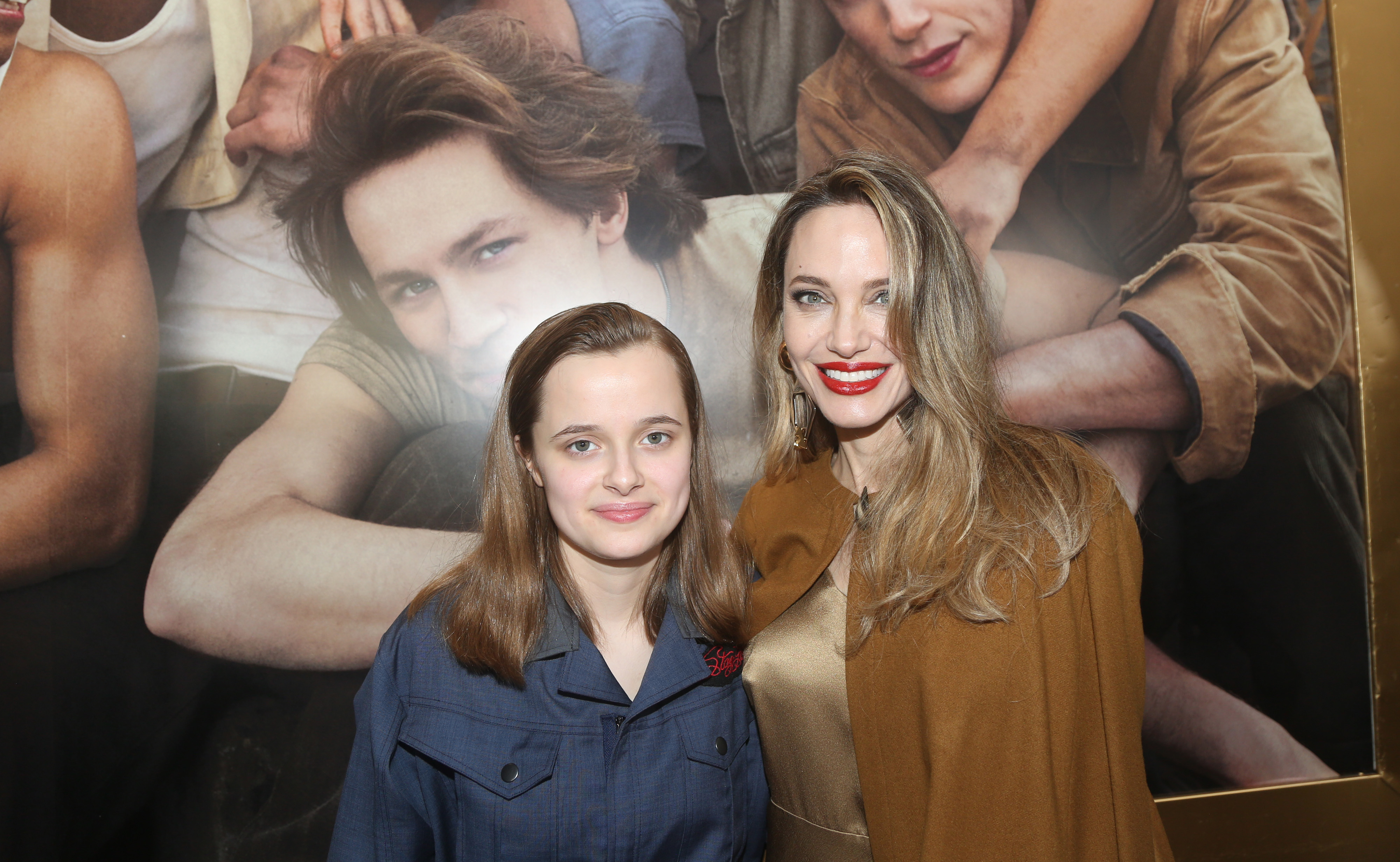 Emily Bader, in a blue blouse, and Erin Richards, in a brown coat, pose together in front of a movie poster background