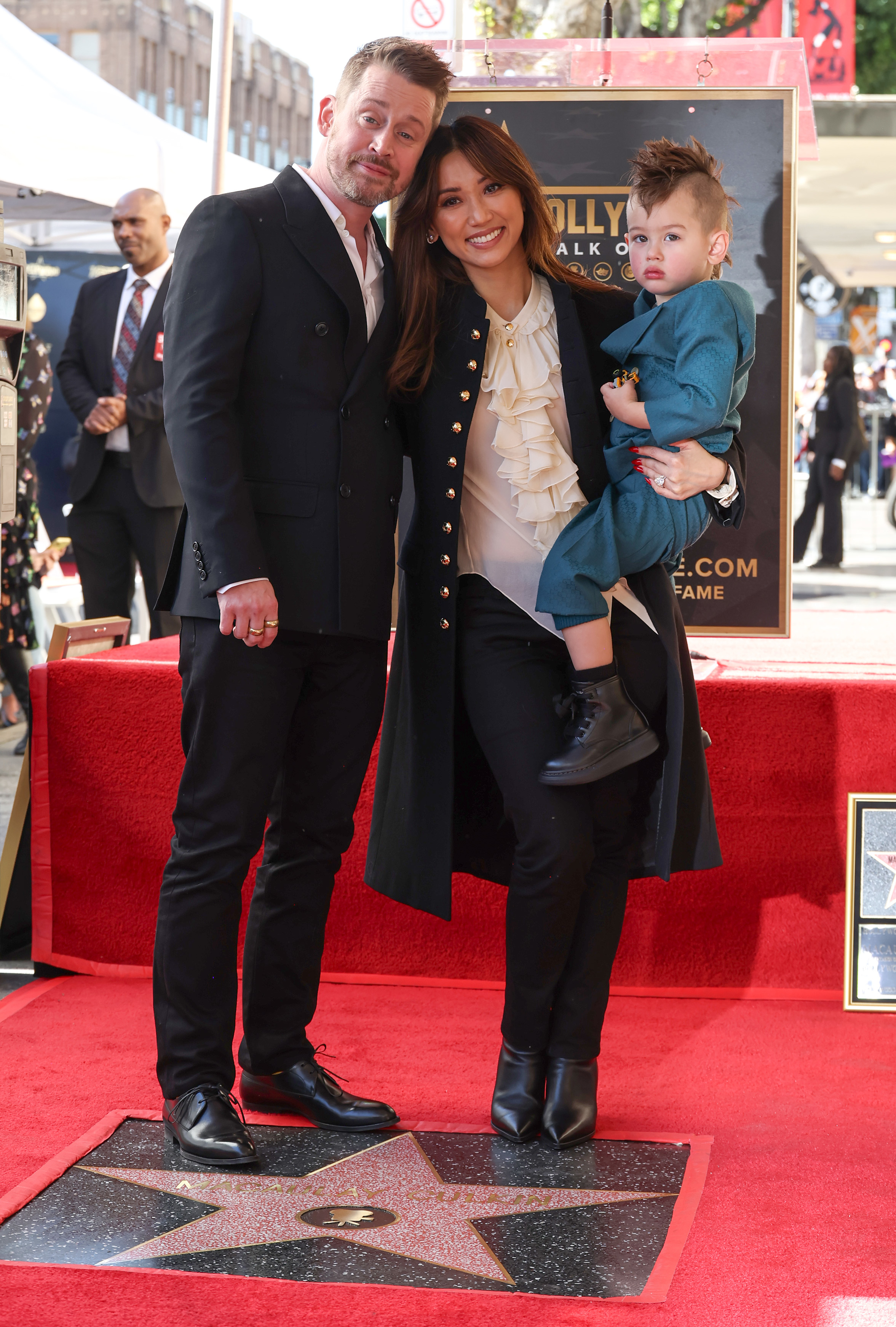 Macaulay Culkin, Brenda Song, and their child pose on the Hollywood Walk of Fame red carpet in elegant attire for Culkin's star ceremony