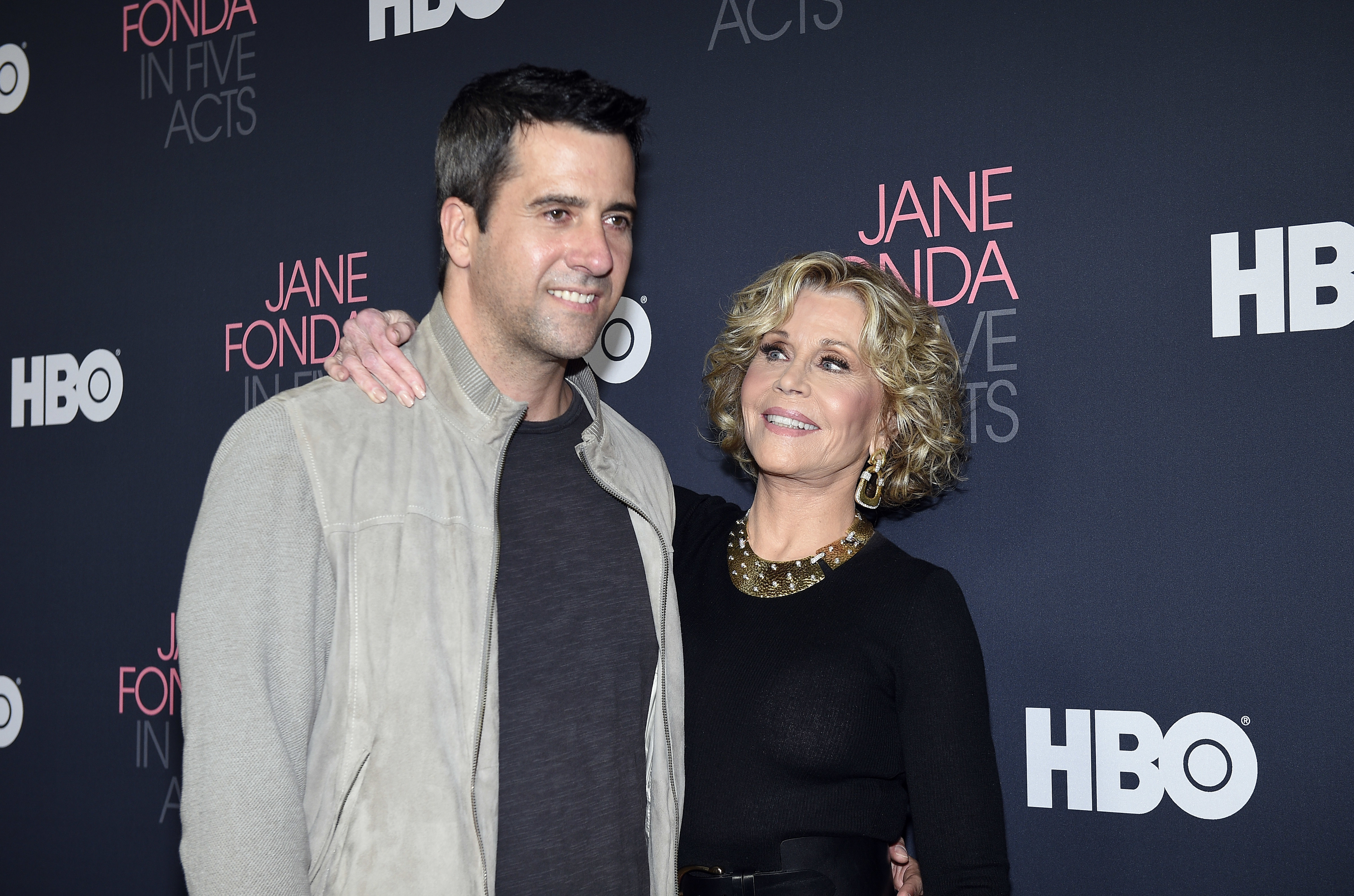 Jane Fonda and Troy Garity posing on the red carpet for the premiere of "Jane Fonda in Five Acts." Jane is wearing a black dress with a statement necklace