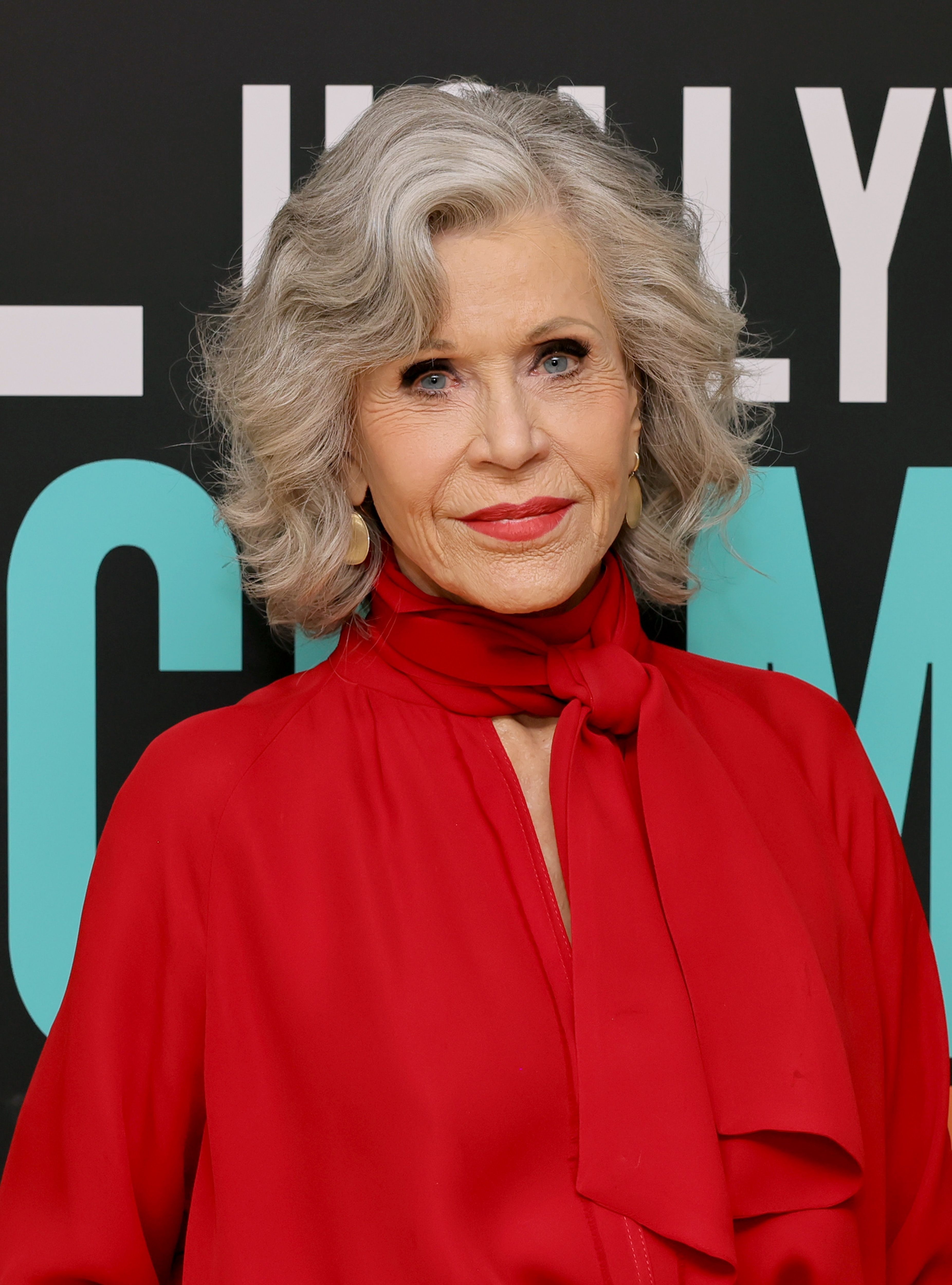 Jane Fonda attends an event wearing a stylish outfit with a high-neck red blouse and a matching scarf