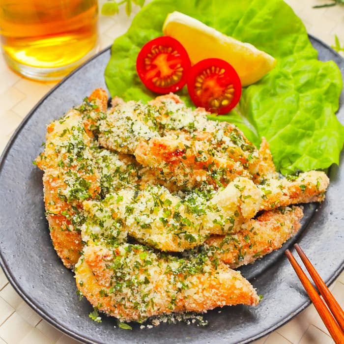 レタスとトマトを添えたハーブとパン粉で覆われた鶏のフィレ。隣にはレモンのくし形が置かれている。