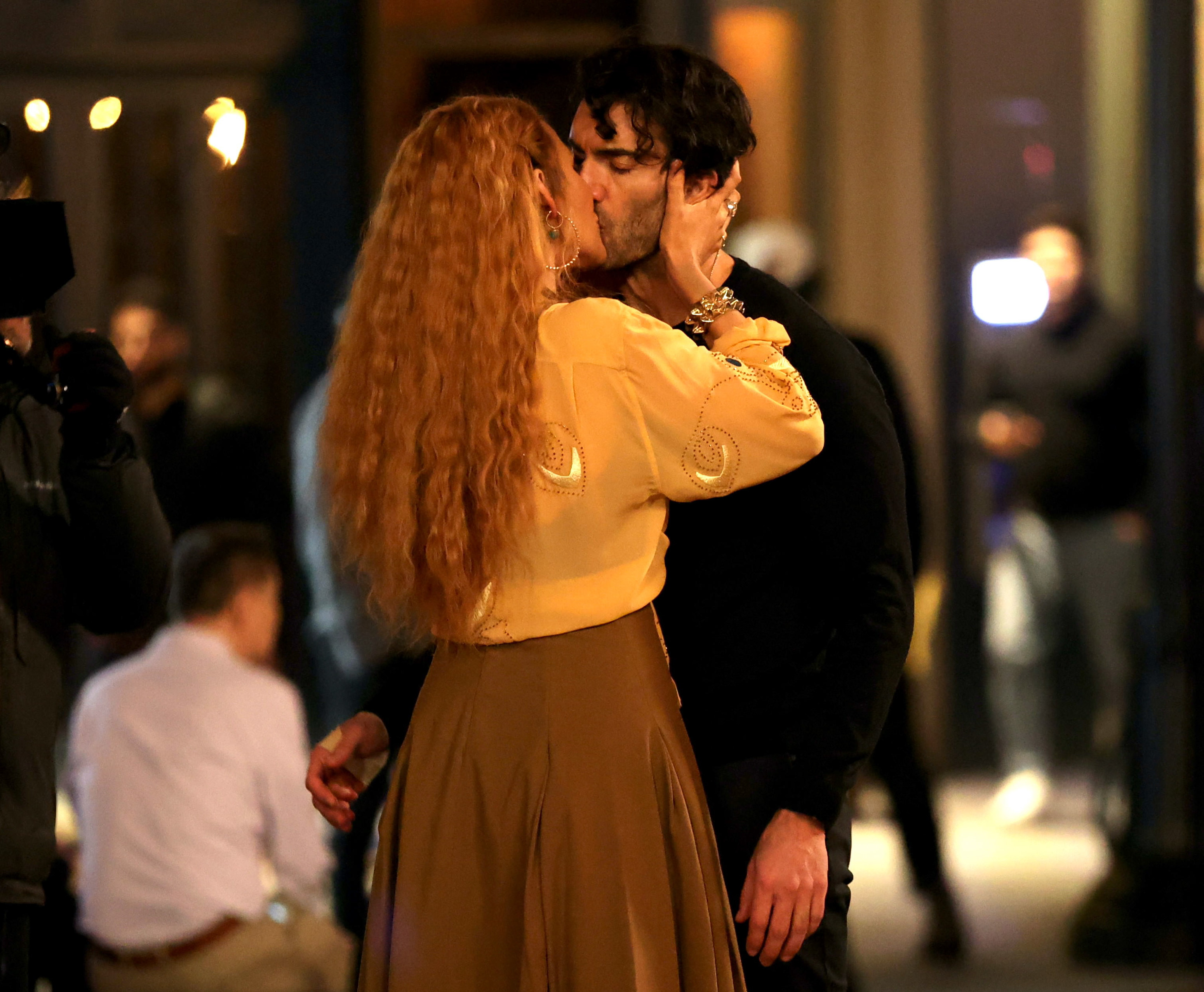 Unknown individuals kissing in a public place, with one person wearing a blouse and skirt and the other wearing a black shirt