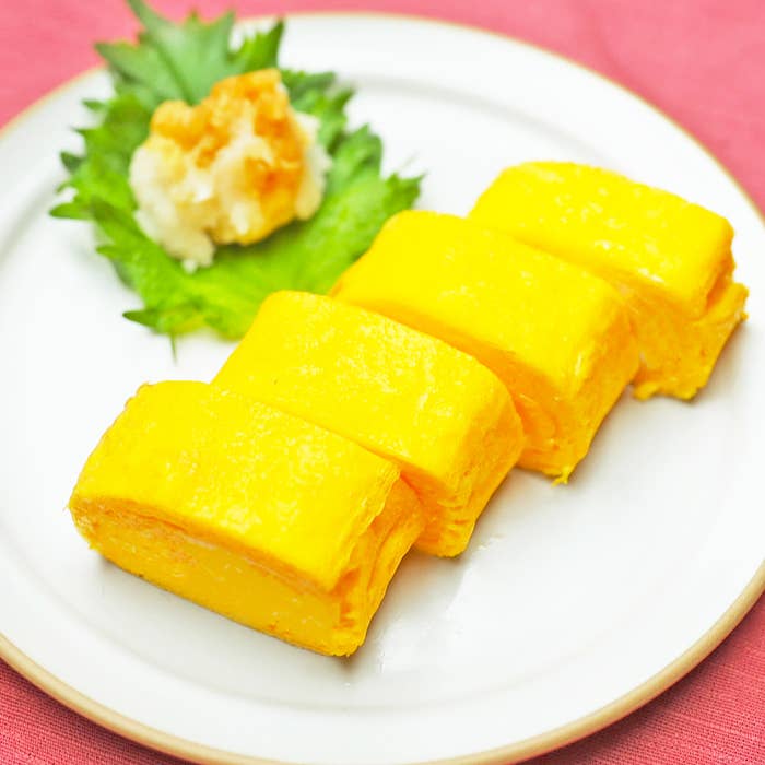 白いプレートに盛り付けられた玉子焼き4切れと青じそとおろし生姜。