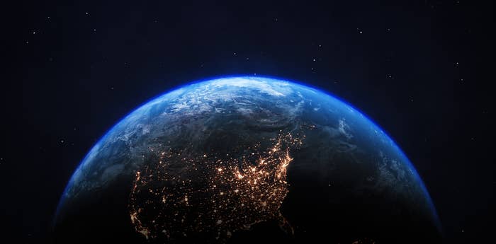 The image shows a view of Earth from space, with visible city lights on the continent and stars in the background