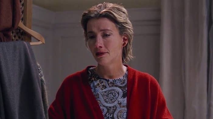 Emma Thompson appears emotional in a scene, wearing a patterned shirt and a red cardigan, set in an indoor space