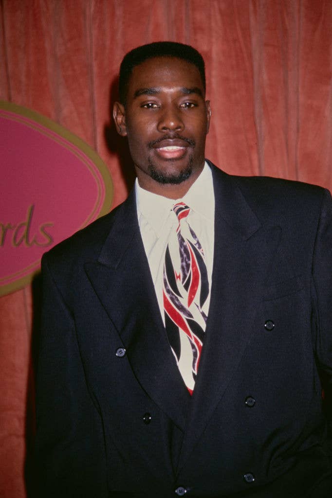 Man posing in a suit with a patterned tie on a red carpet