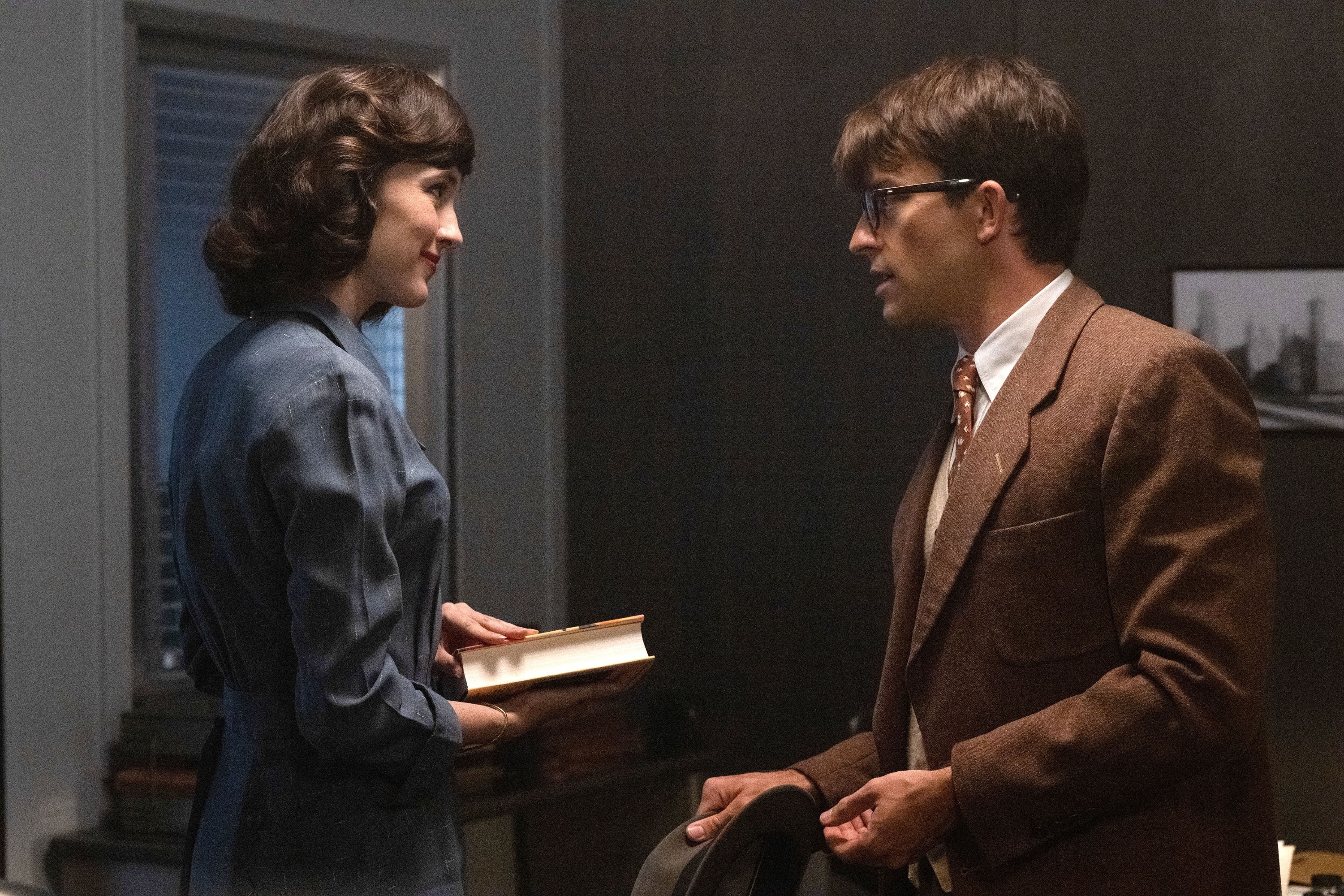 Rachel Brosnahan and Michael Zegen in a scene from "The Marvelous Mrs. Maisel," with Rachel holding a book and Michael wearing a brown suit and glasses