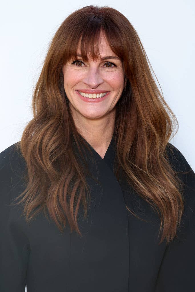 Julia Roberts smiling, wearing a black top with long wavy hair styled loosely