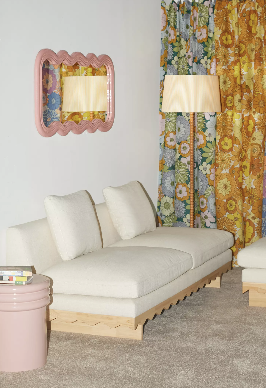 Modern surviving  country   setup with a pick  sofa, floral curtains, a pinkish  scalloped mirror, a level  lamp, and a broadside  array  with books. The representation  highlights location  decor