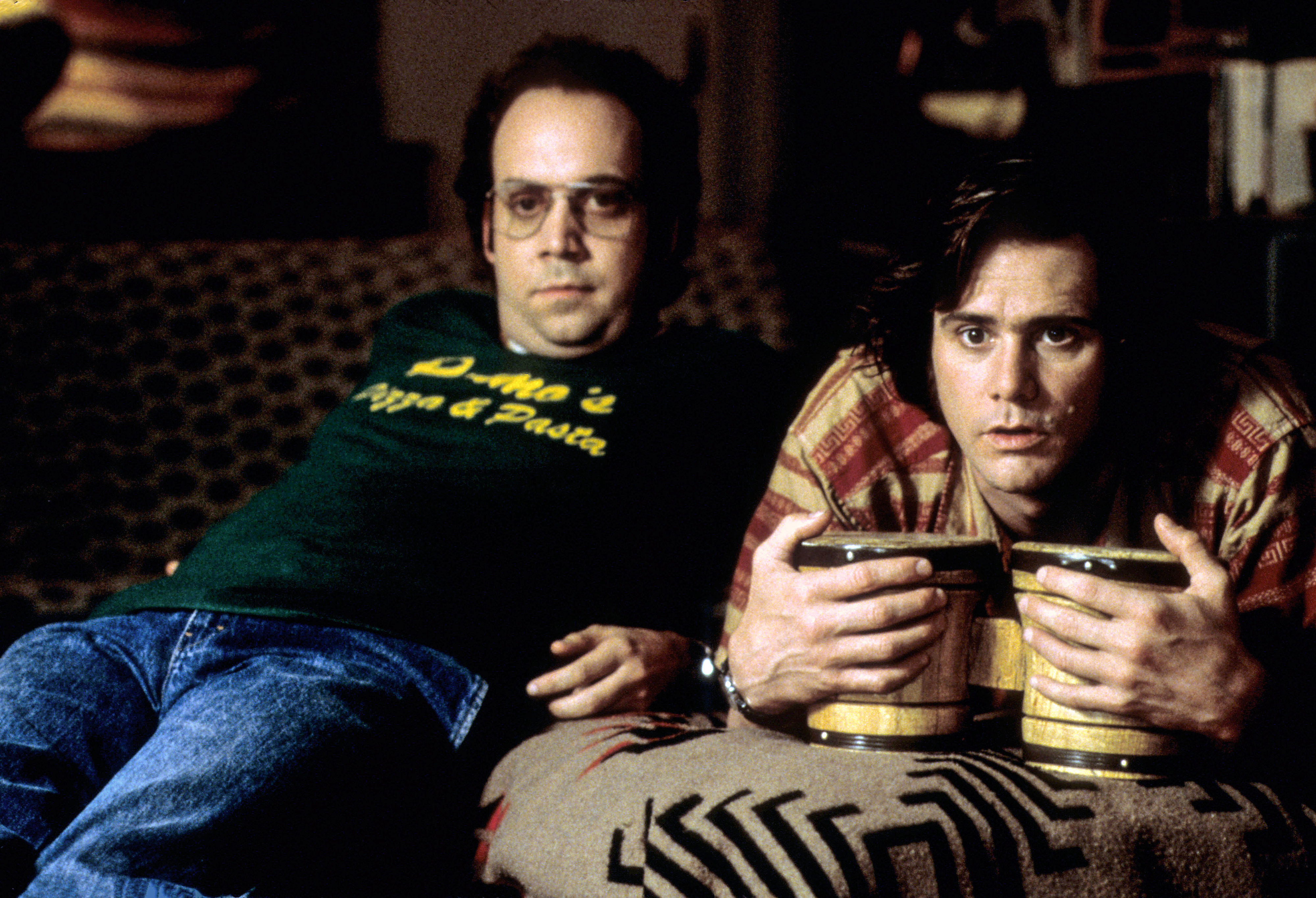 Paul Giamatti and Jim Carrey sit on a couch. Jim Carrey holds bongo drums