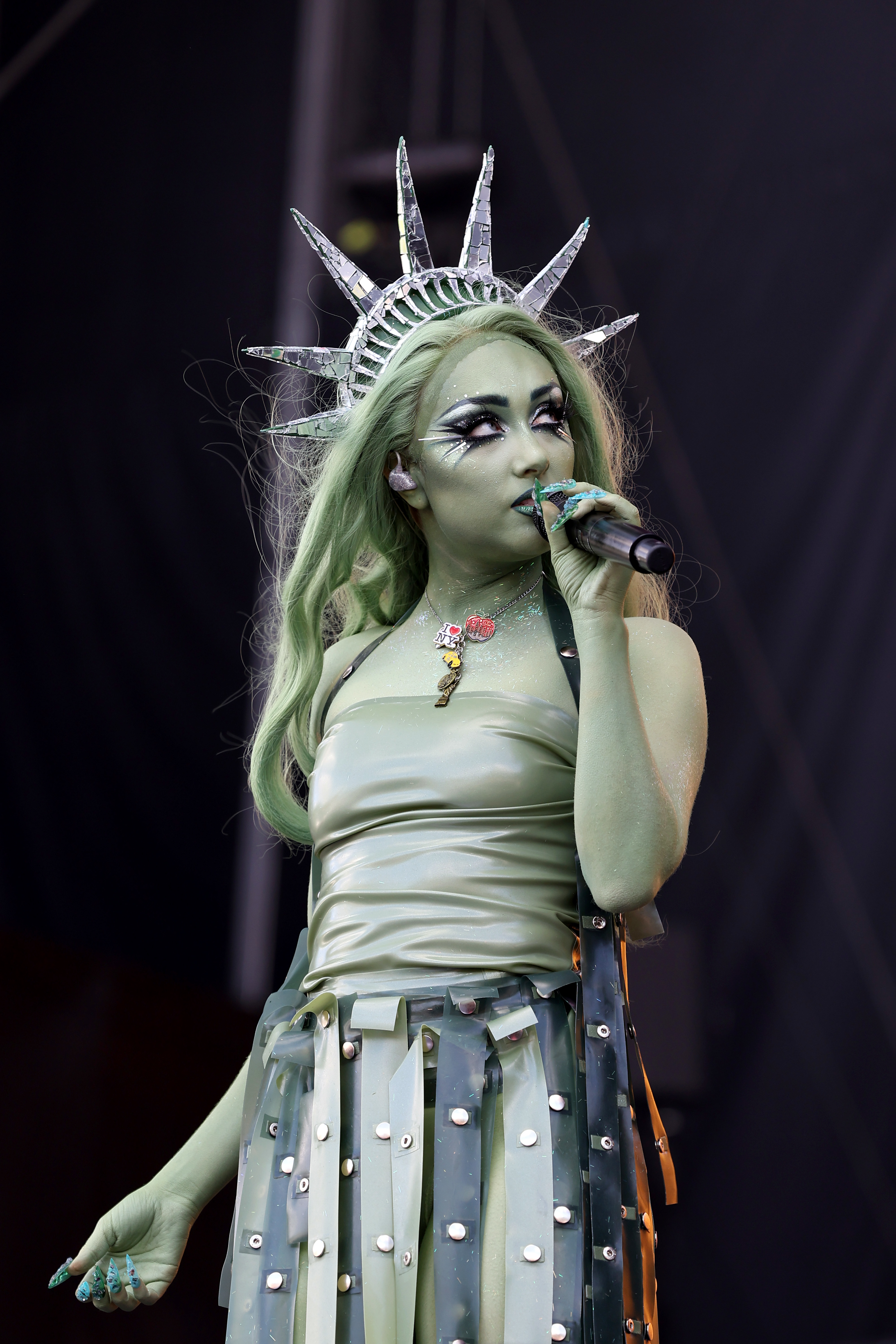 Chappell Roan in a Statue of Liberty-themed outfit with a crown and microphone performing on stage