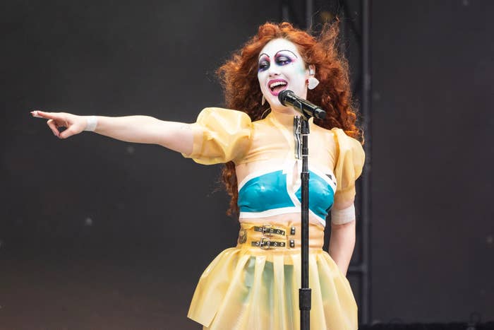 Chappell Roan with exaggerated makeup and hair performs on stage, wearing a bold, distinctive outfit with exaggerated shoulders and a fitted bodice