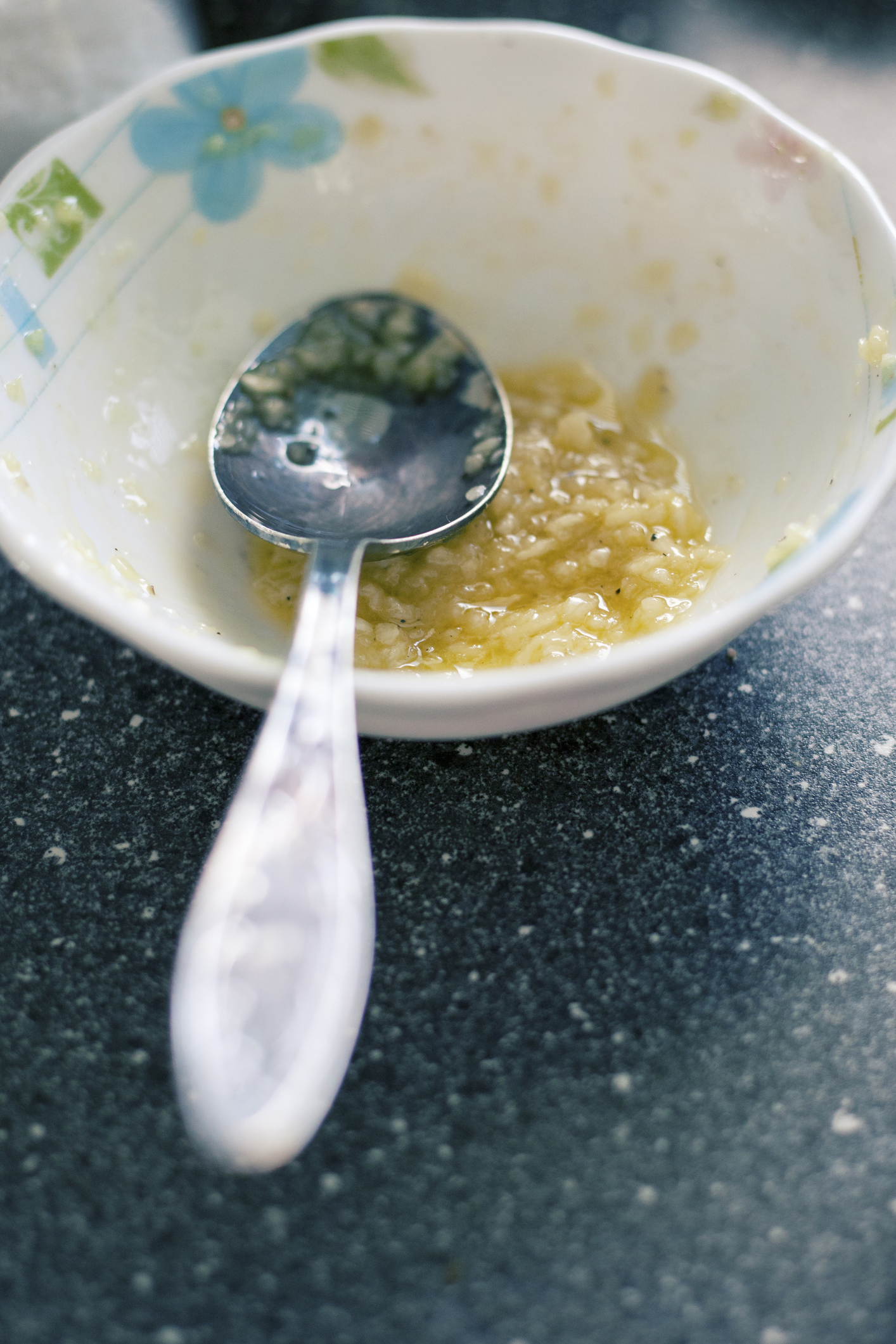 A small bowl with mashed banana and a spoon resting in it. The bowl has a floral design. The setting appears to be a kitchen countertop