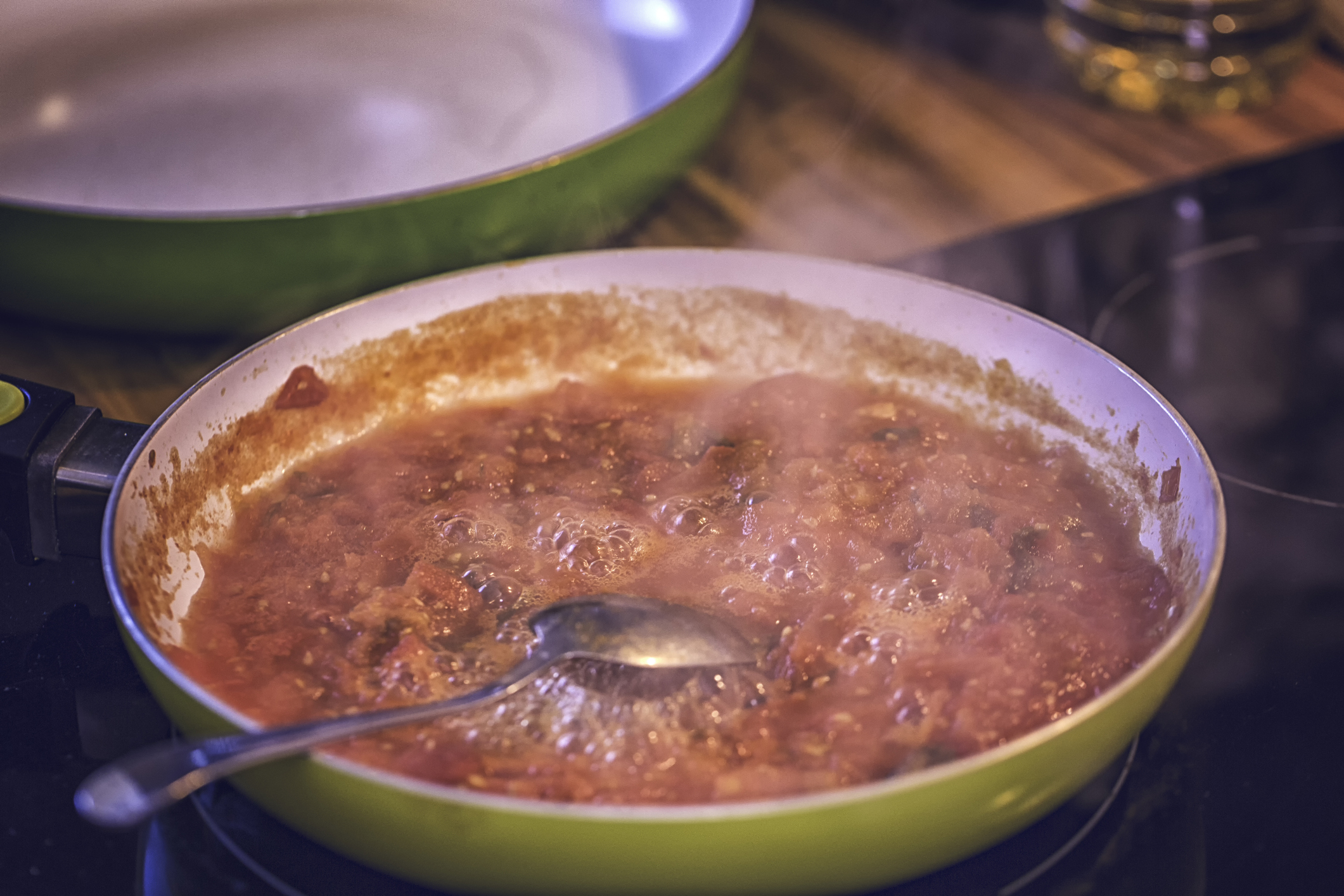 A pan of tomato sauce simmers with a metal spoon resting in it on a stovetop