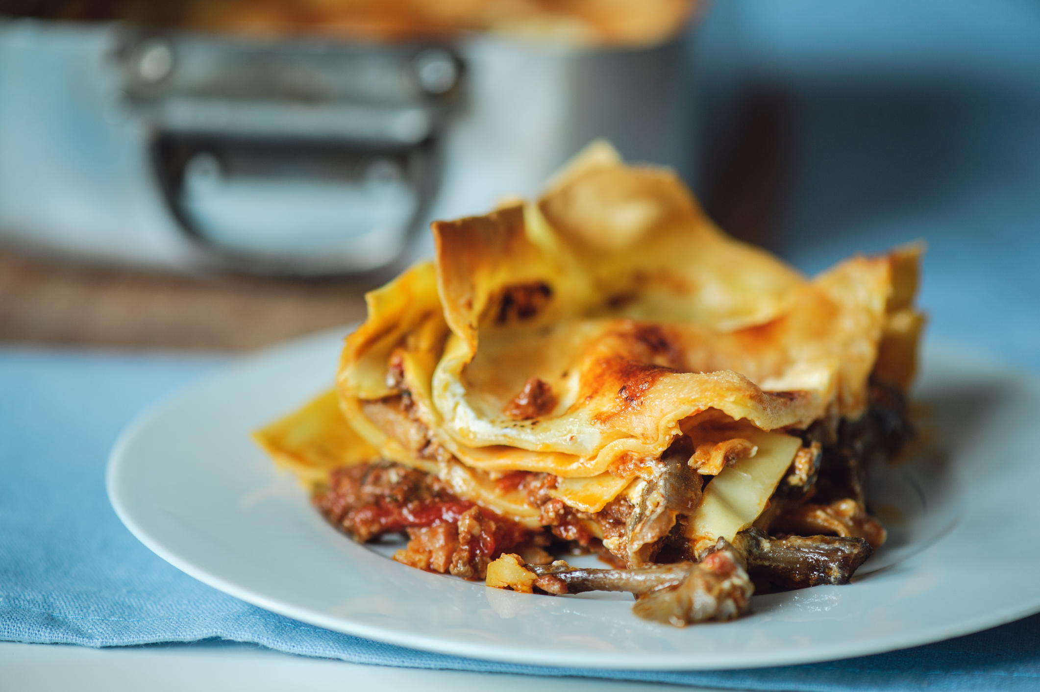 A plate of lasagna with layers of pasta, meat, and sauce, placed on a table with a baking dish of lasagna in the background