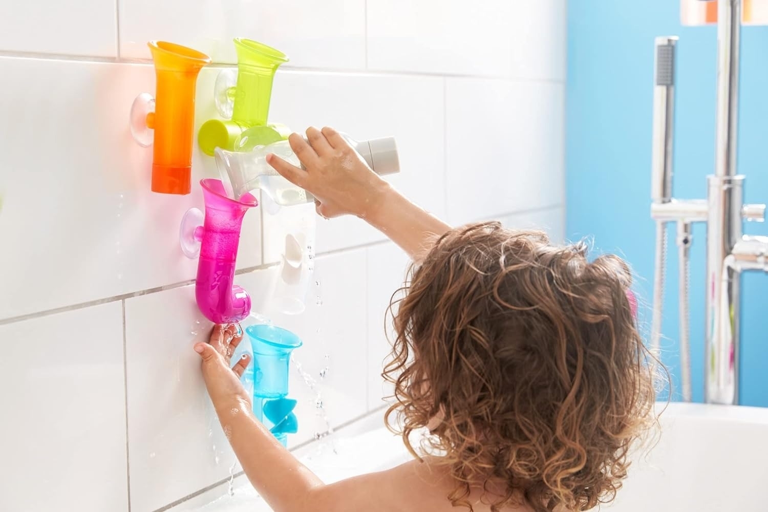 Child playing with colorful bath toys attached to a white tiled wall in a bathroom