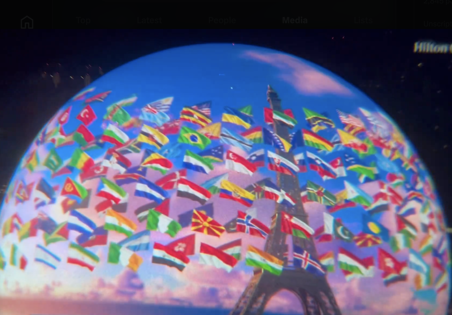 The image shows the Eiffel Tower with flags from various countries around the world surrounding it, creating a scene of global unity