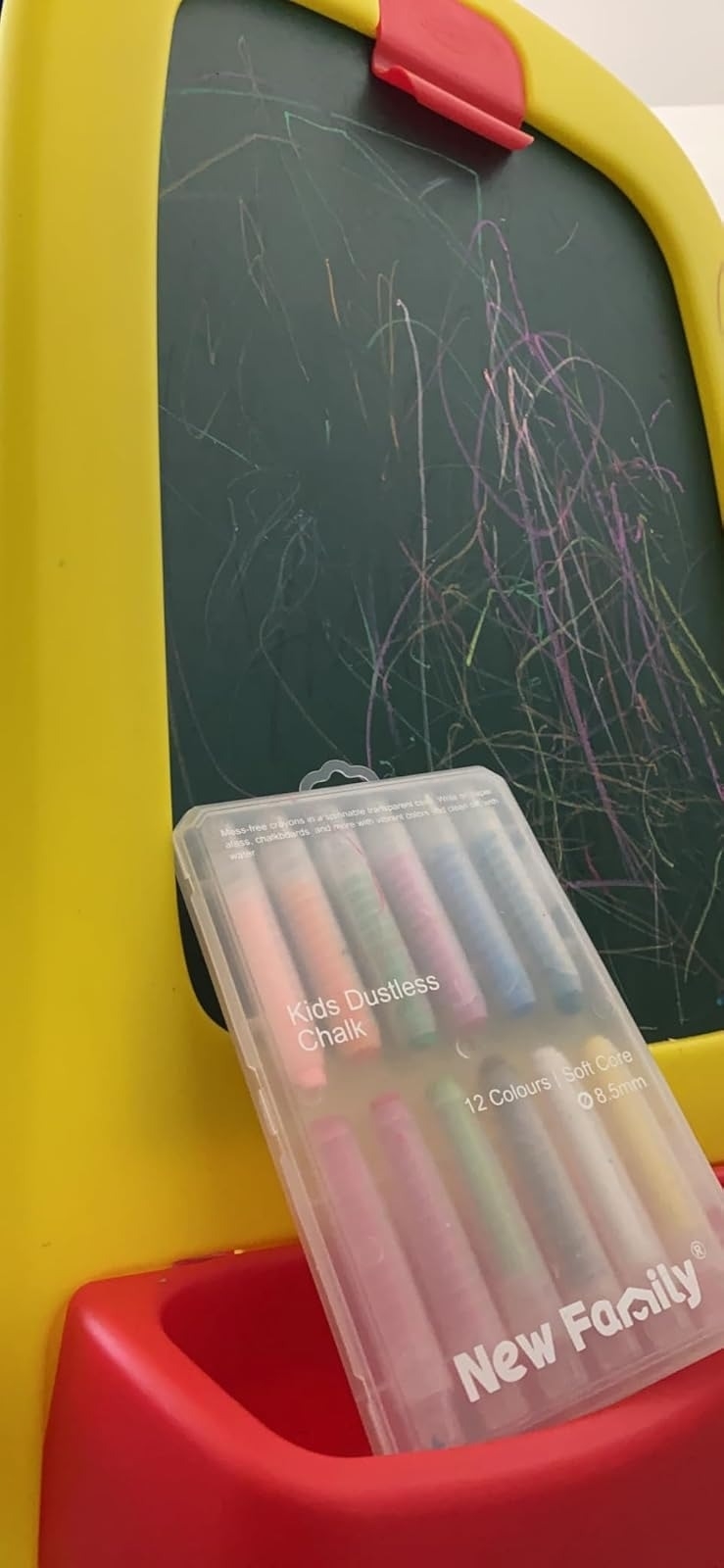 Kids chalkboard easel with colorful scribbles. A package of 12 dustless chalks labeled &quot;New Family&quot; is placed in the easel's tray