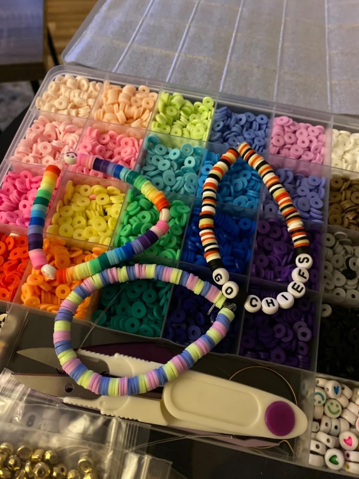 Assortment of colorful beads in a storage case with three DIY bracelets and crafting tools. One bracelet reads &quot;GO CHIEFS&quot;