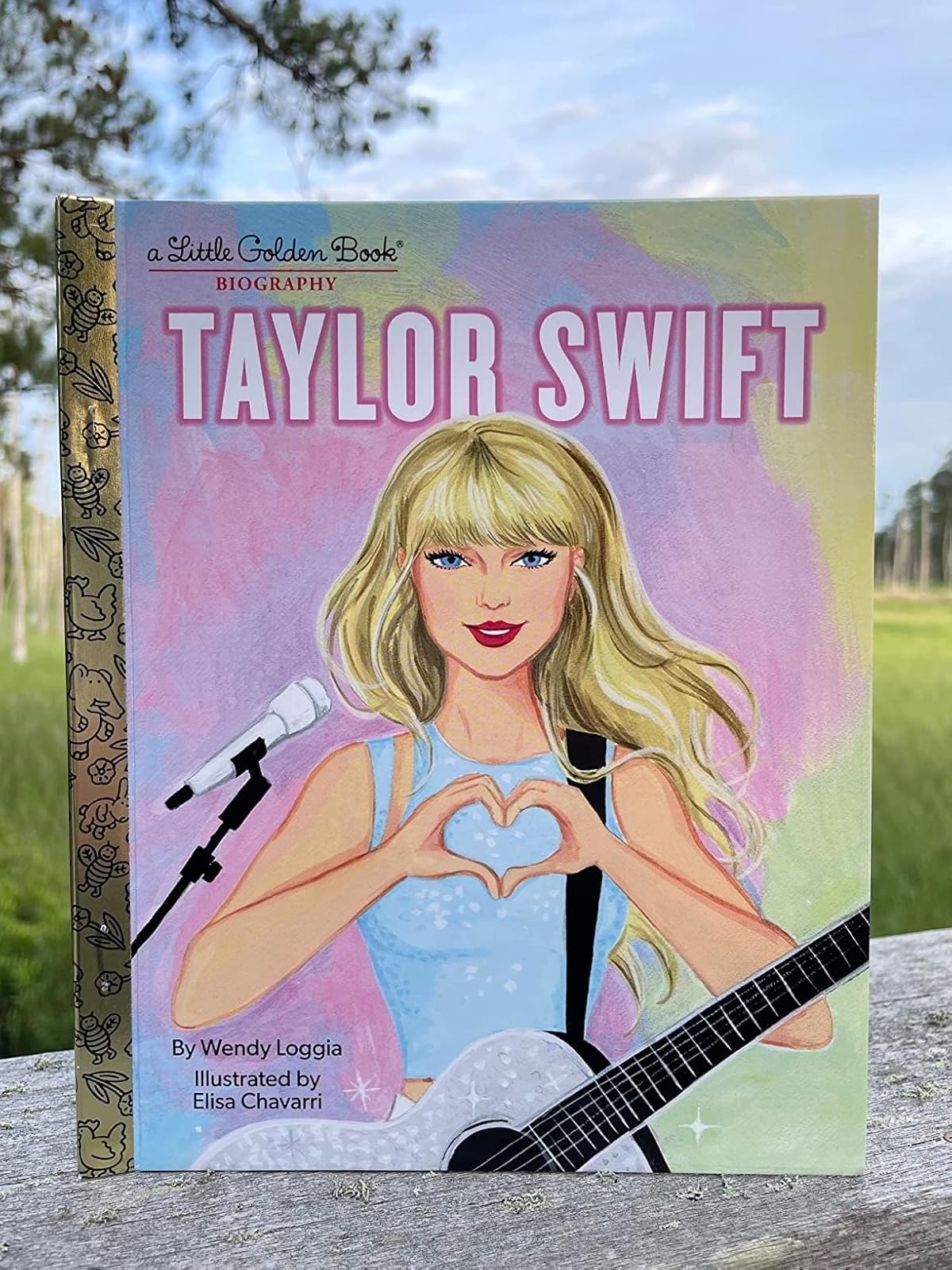 Cover of &quot;Little Golden Book Biography: Taylor Swift&quot; by Wendy Loggia, illustrated by Elisa Chavarri, featuring an illustrated Taylor Swift holding a guitar and making a heart gesture with her hands