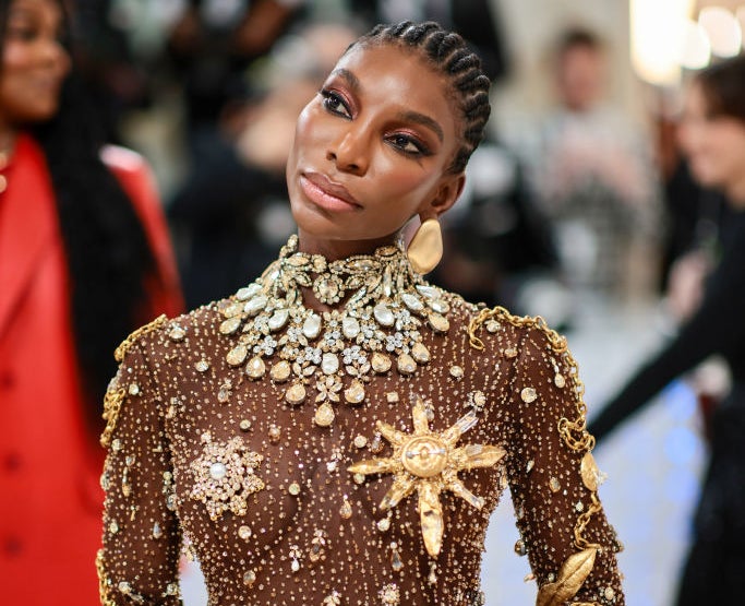 Michaela Coel in an ornate, jewel-embellished gown with intricate metallic designs at a red carpet event