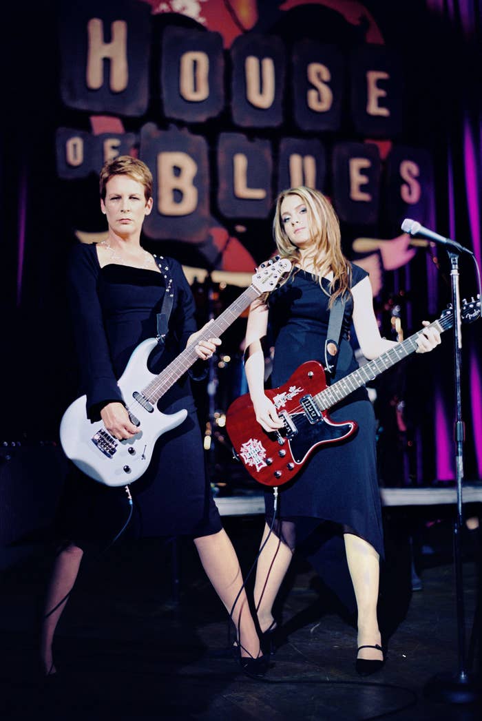 Jamie Lee Curtis and Lindsay Lohan playing guitars on stage at House of Blues, wearing elegant black dresses
