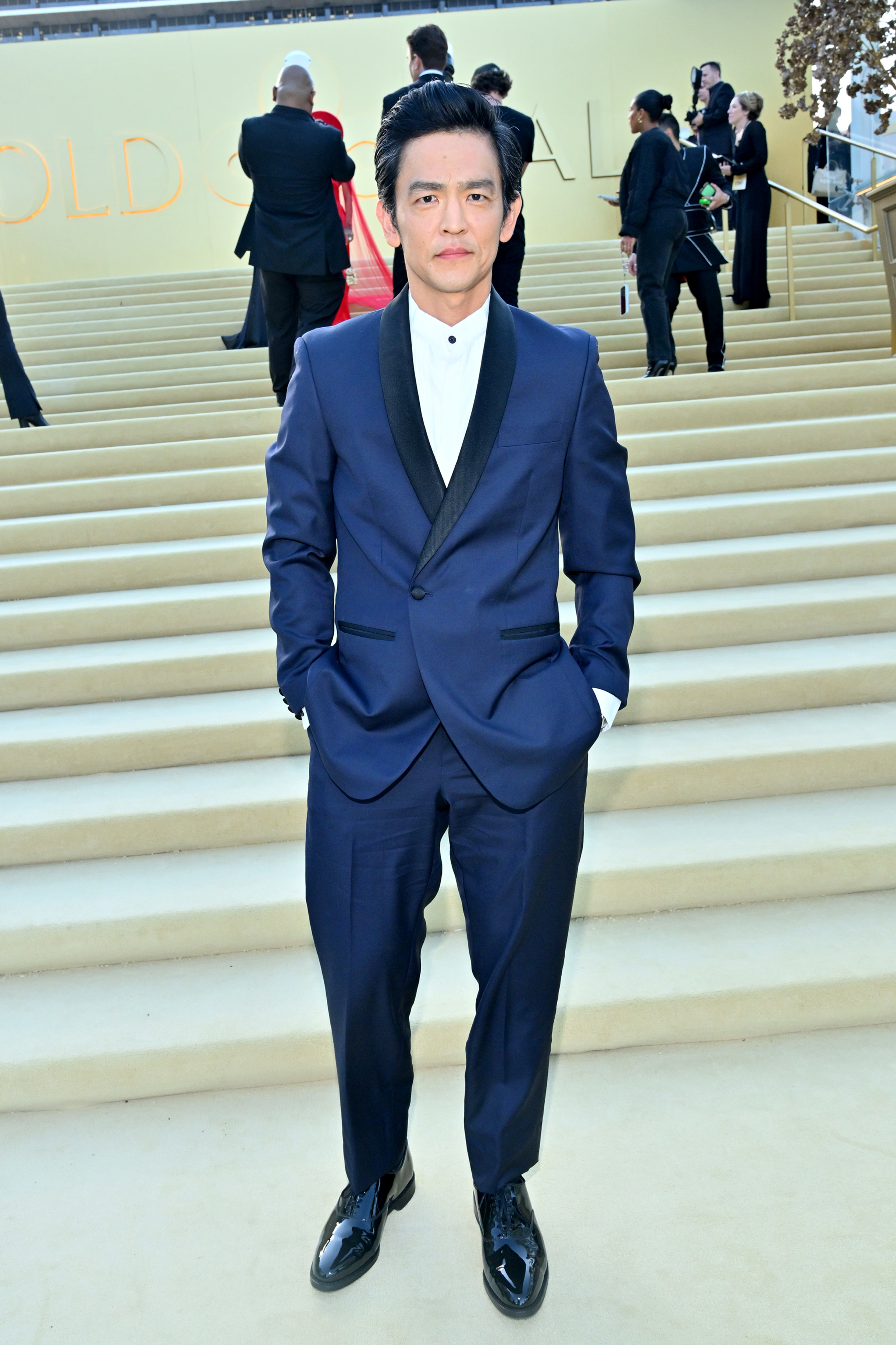 John Cho poses on staircase in a formal suit and black dress shoes