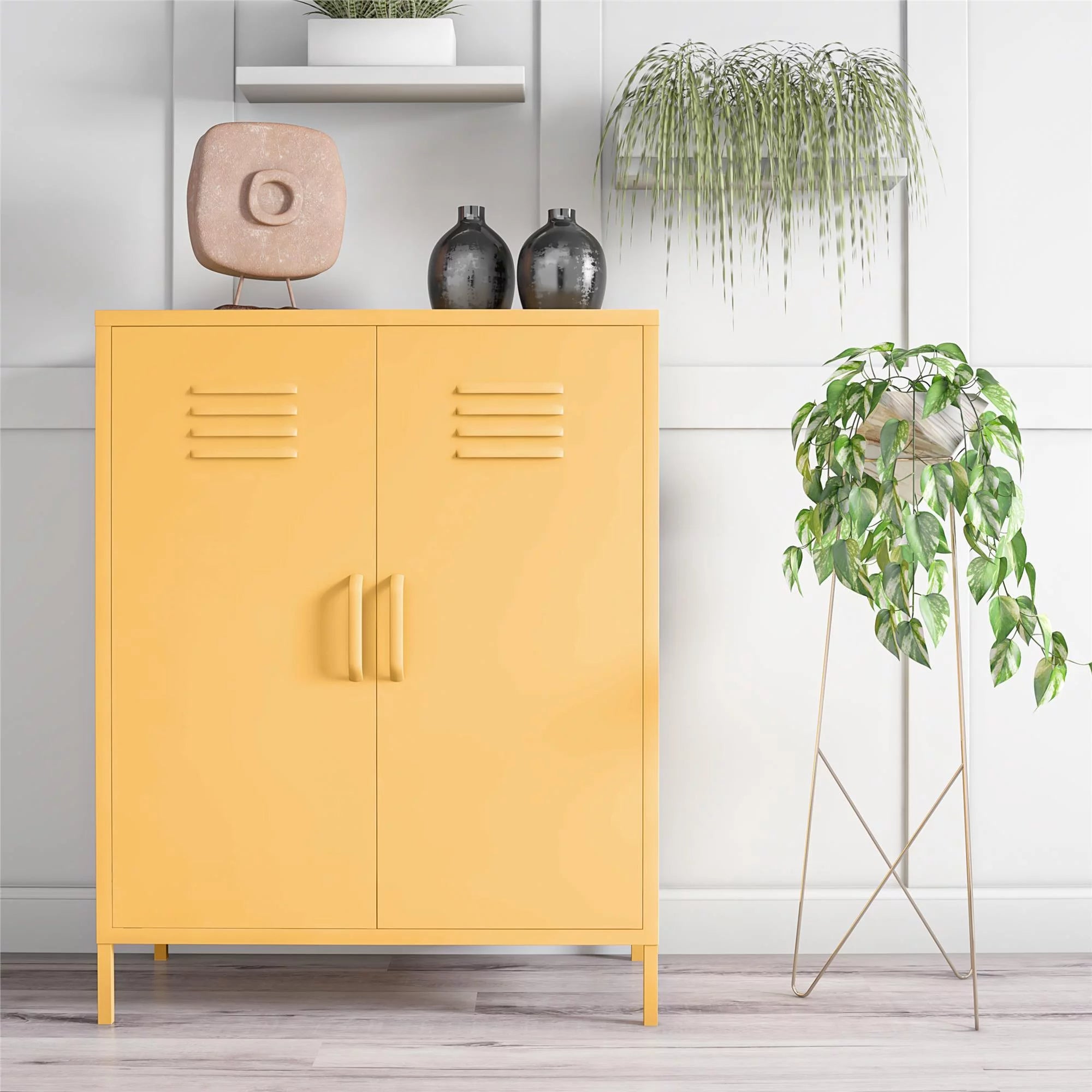 Kabinet kuning dengan pegangan ganda, vas dekoratif, dan patung batu di atasnya. Tanaman pot tinggi di atas dudukan dan tanaman gantung dalam ruangan di dekatnya