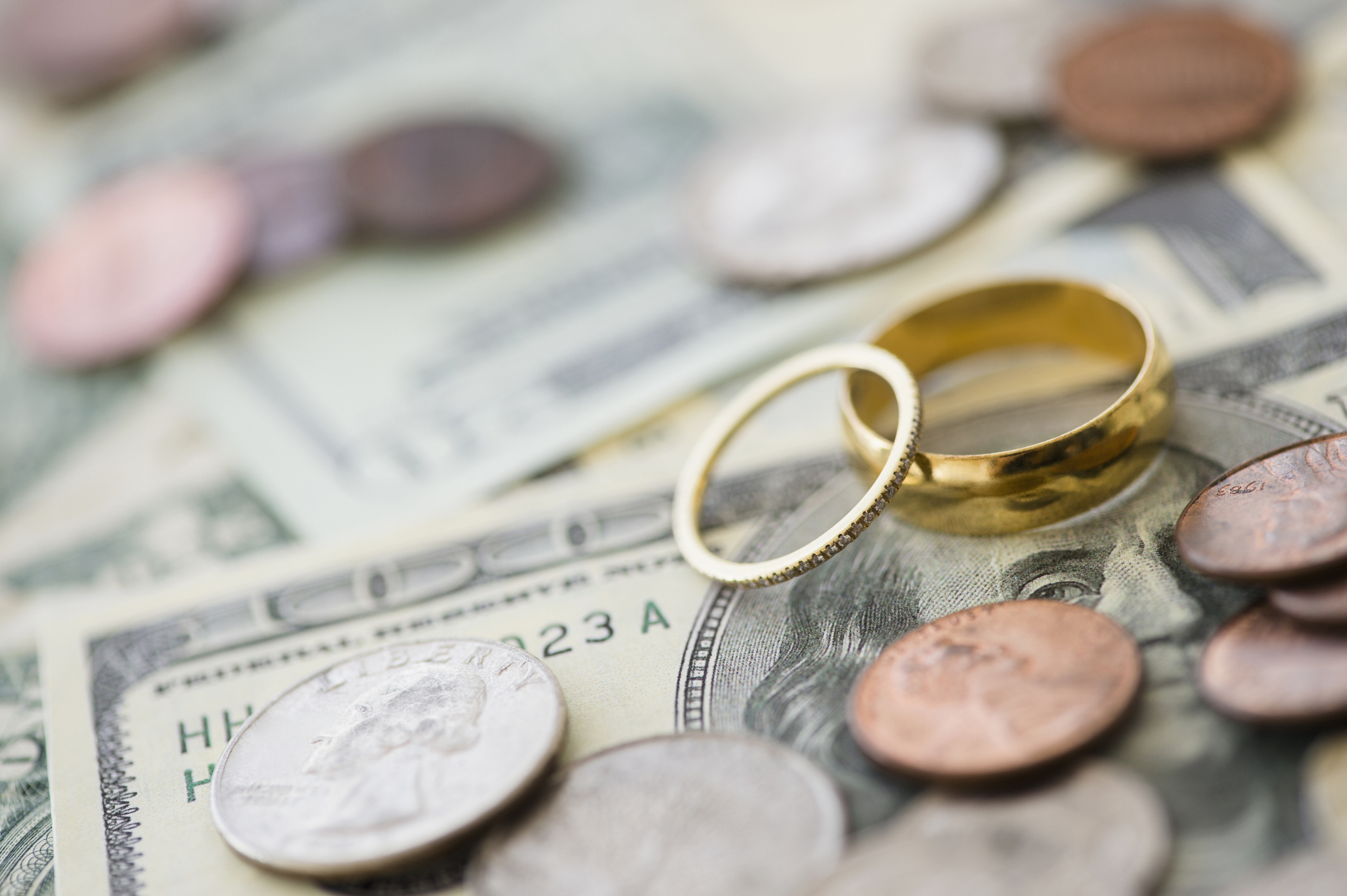 Two wedding rings resting on top of dollar bills and various coins