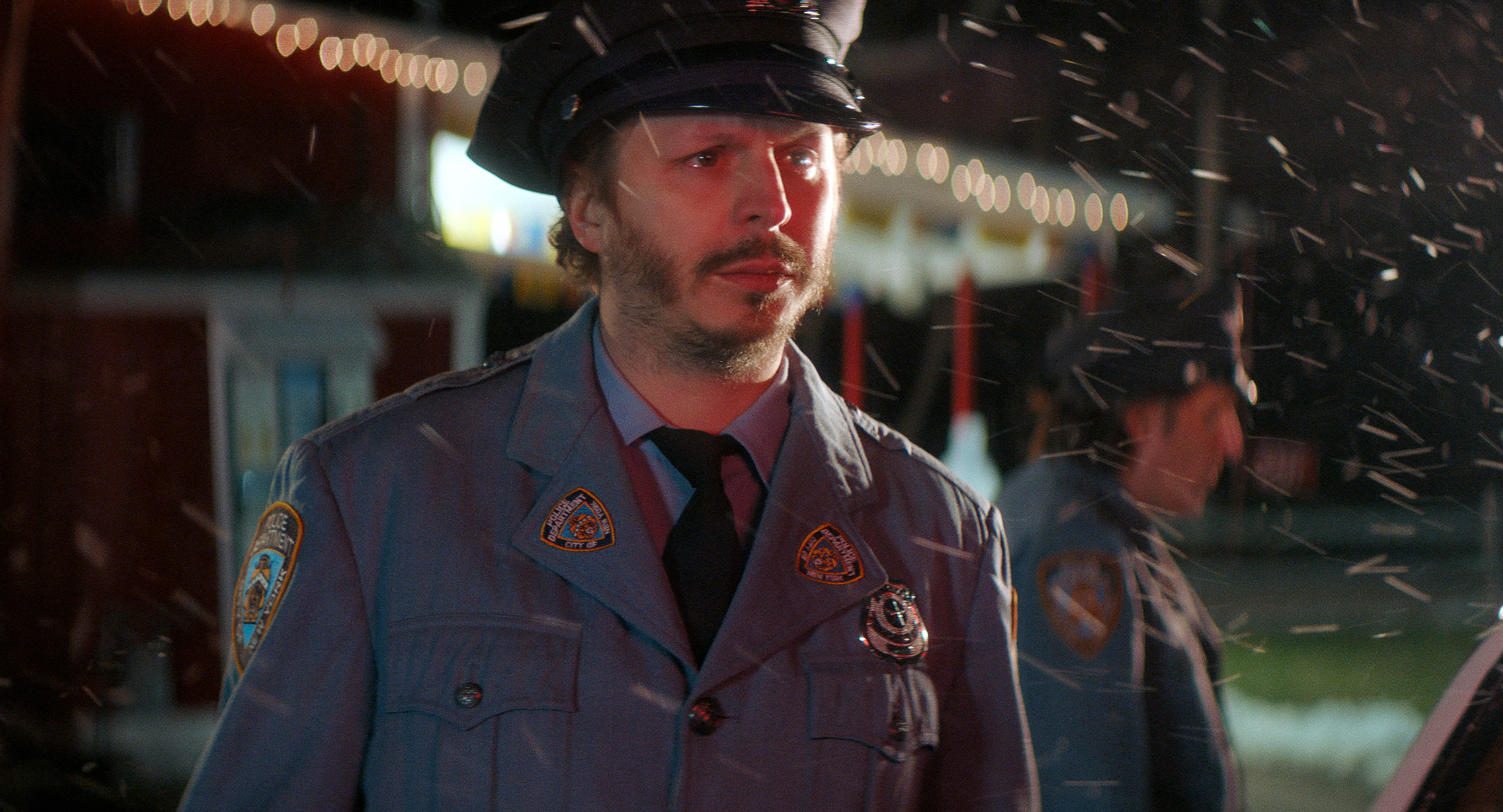Steve Buscemi, in a police uniform, stands in the snow. Another person in uniform is in the background, slightly out of focus