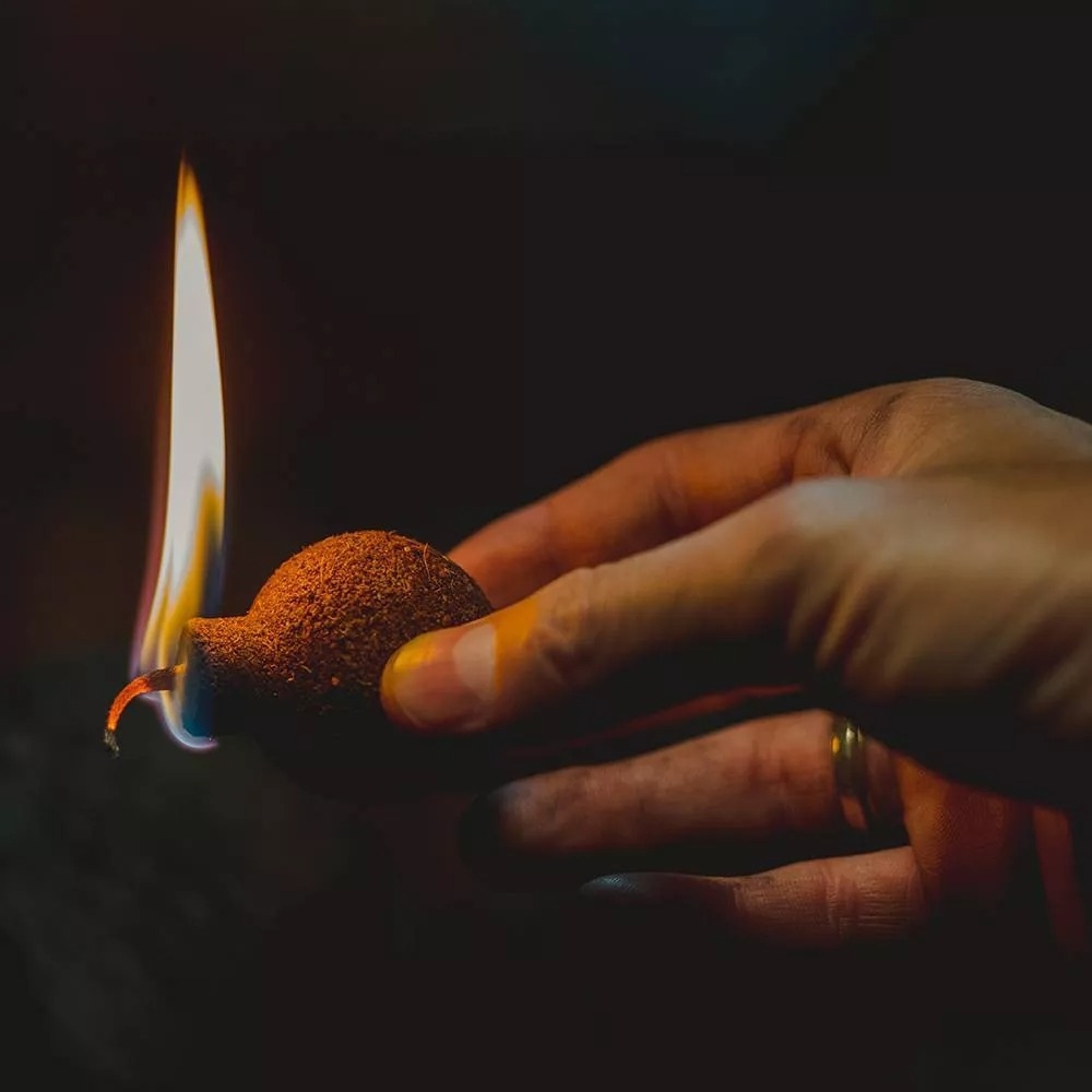 A hand holding a lit firestarter that's shaped like a cartoon bomb