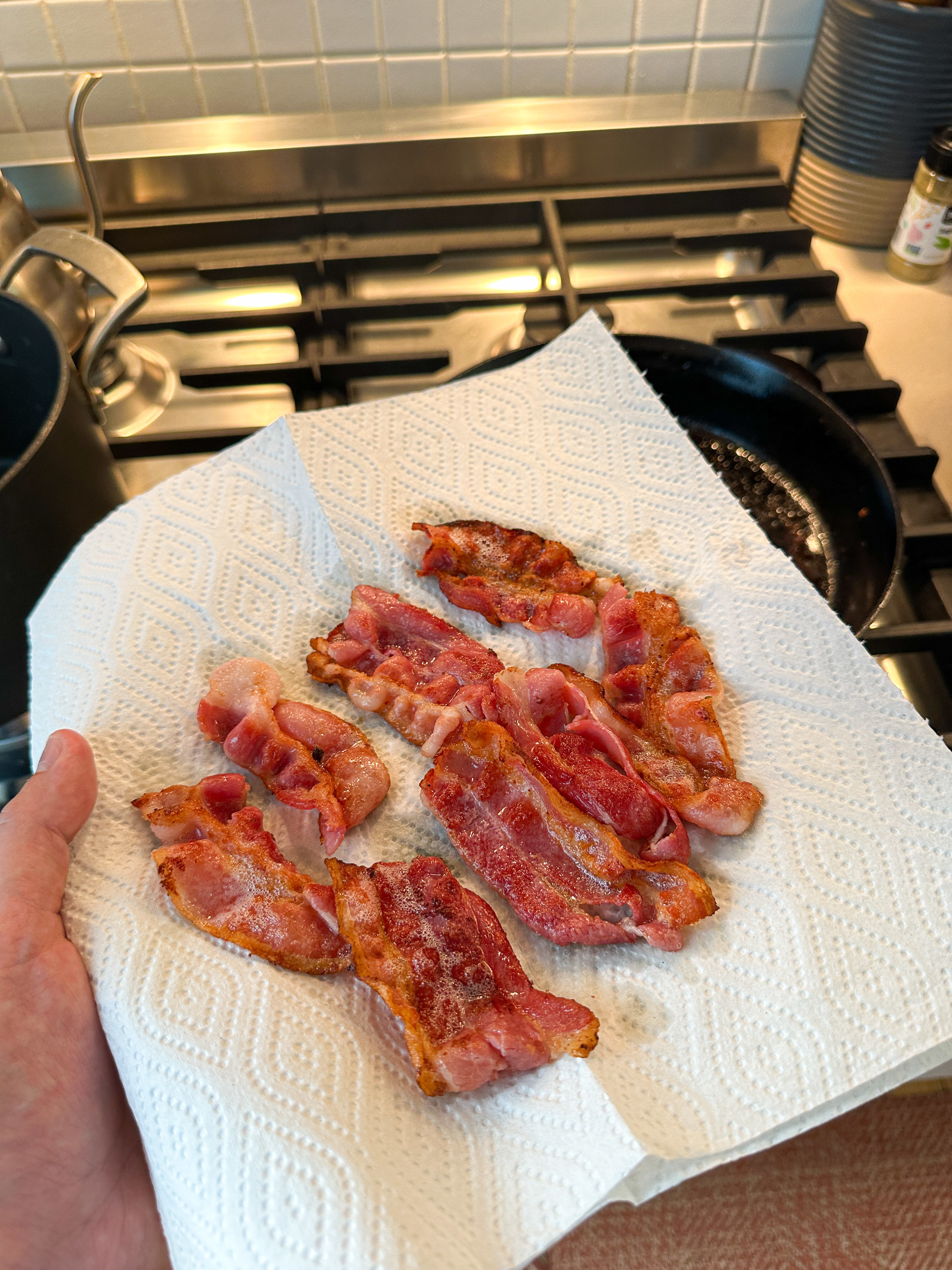 A person holds a paper towel with several crispy bacon strips in a kitchen