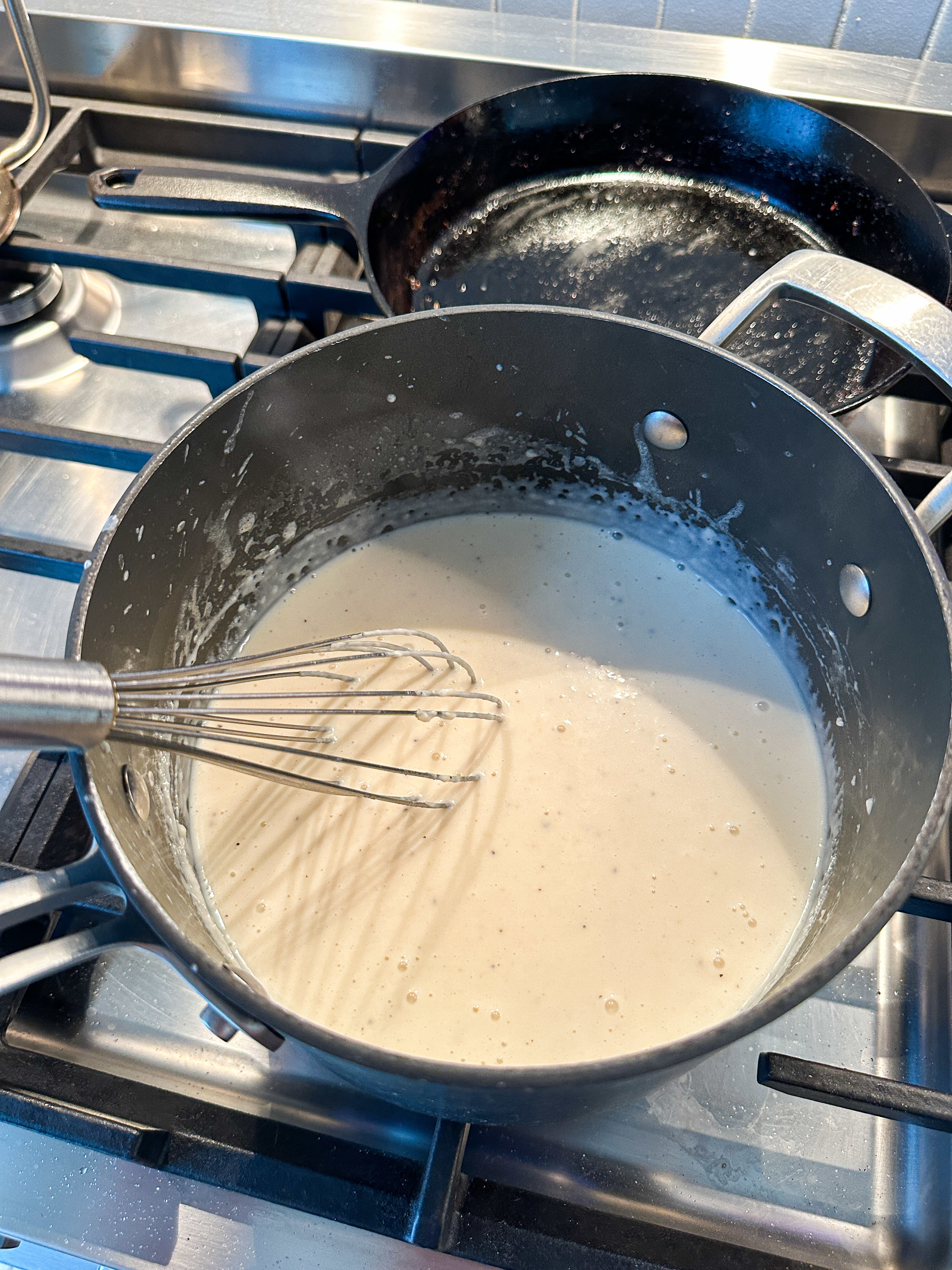 A pot of sauce being whisked on a stove