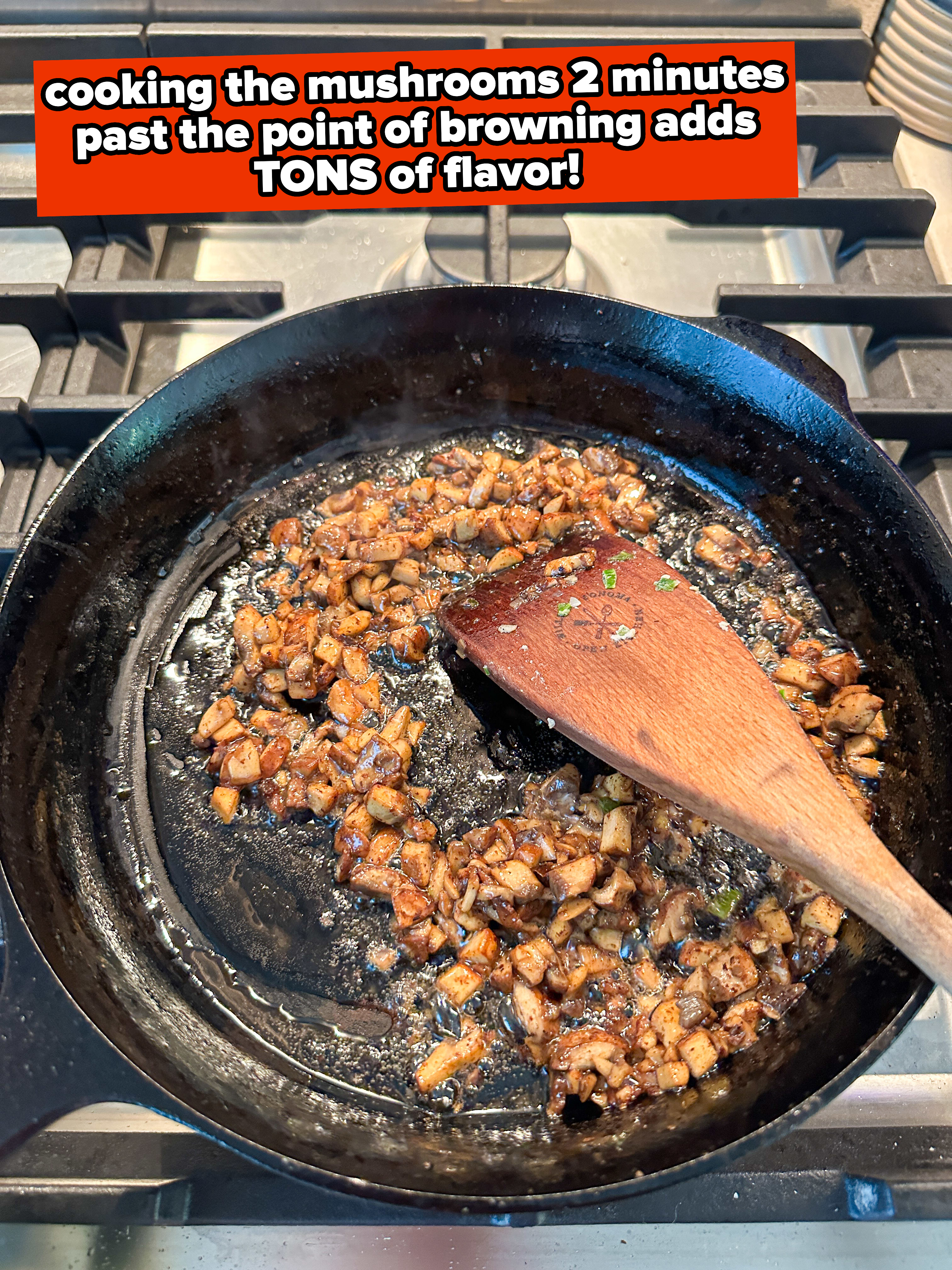 A cast iron skillet with sautéed diced mushrooms being stirred with a wooden spoon on a stovetop